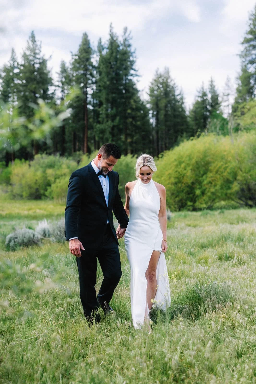 Bride and groom walking hand in hand through a Lake Tahoe meadow.jpg