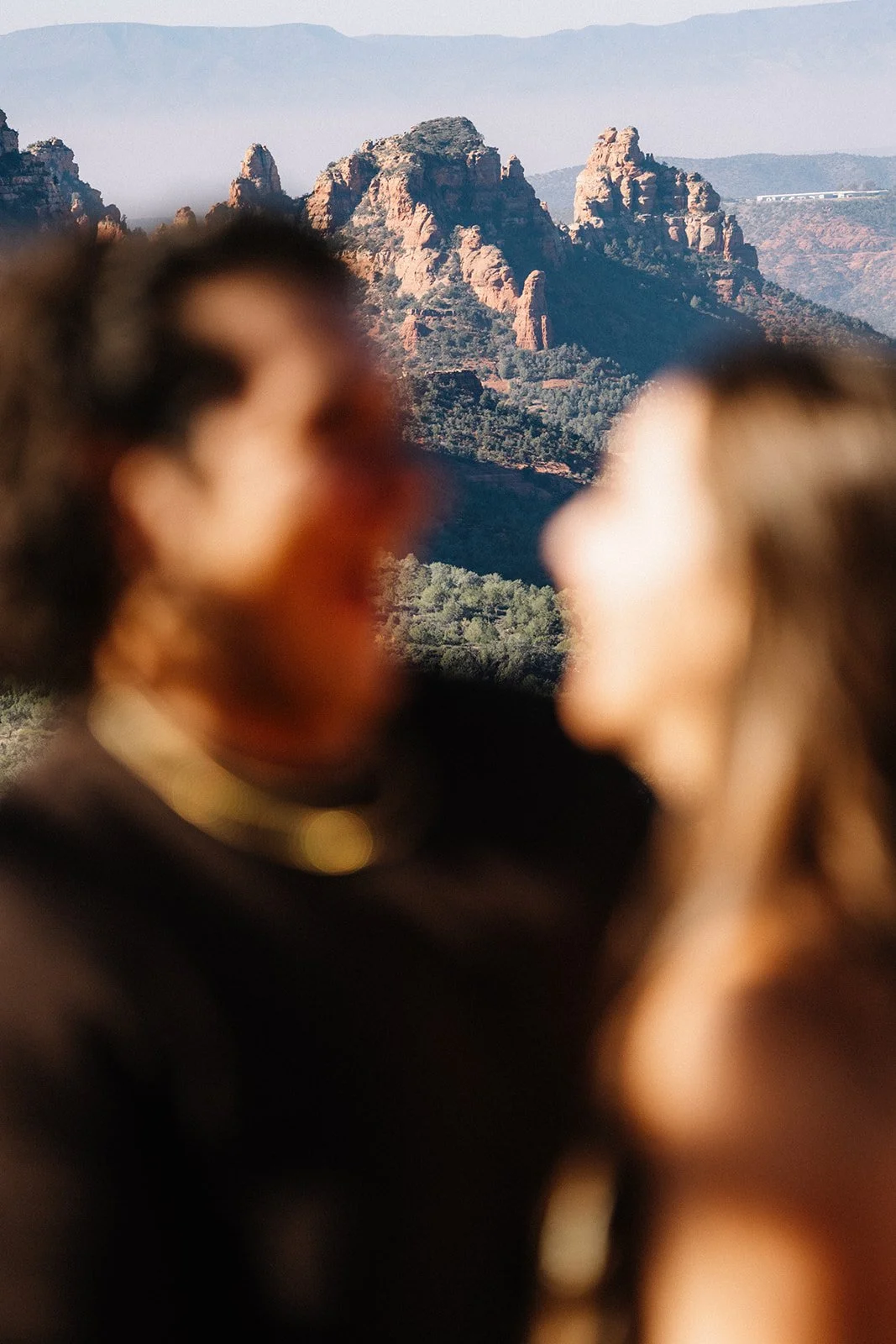 Blurred close-up of two people facing each other with a mountain landscape in the background.