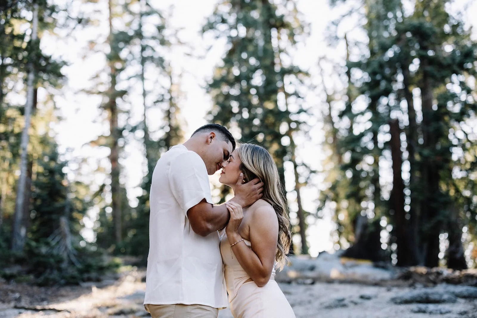 Couple embracing in the forest at Taft Point in Yosemite, foreheads touching as the man gently holds her face