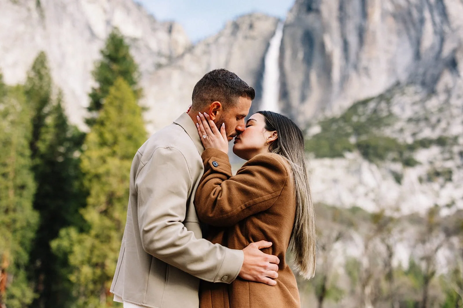 Couple kissing at Cathedral Meadow in Yosemite during their engagement session, mountains and trees framing the scene