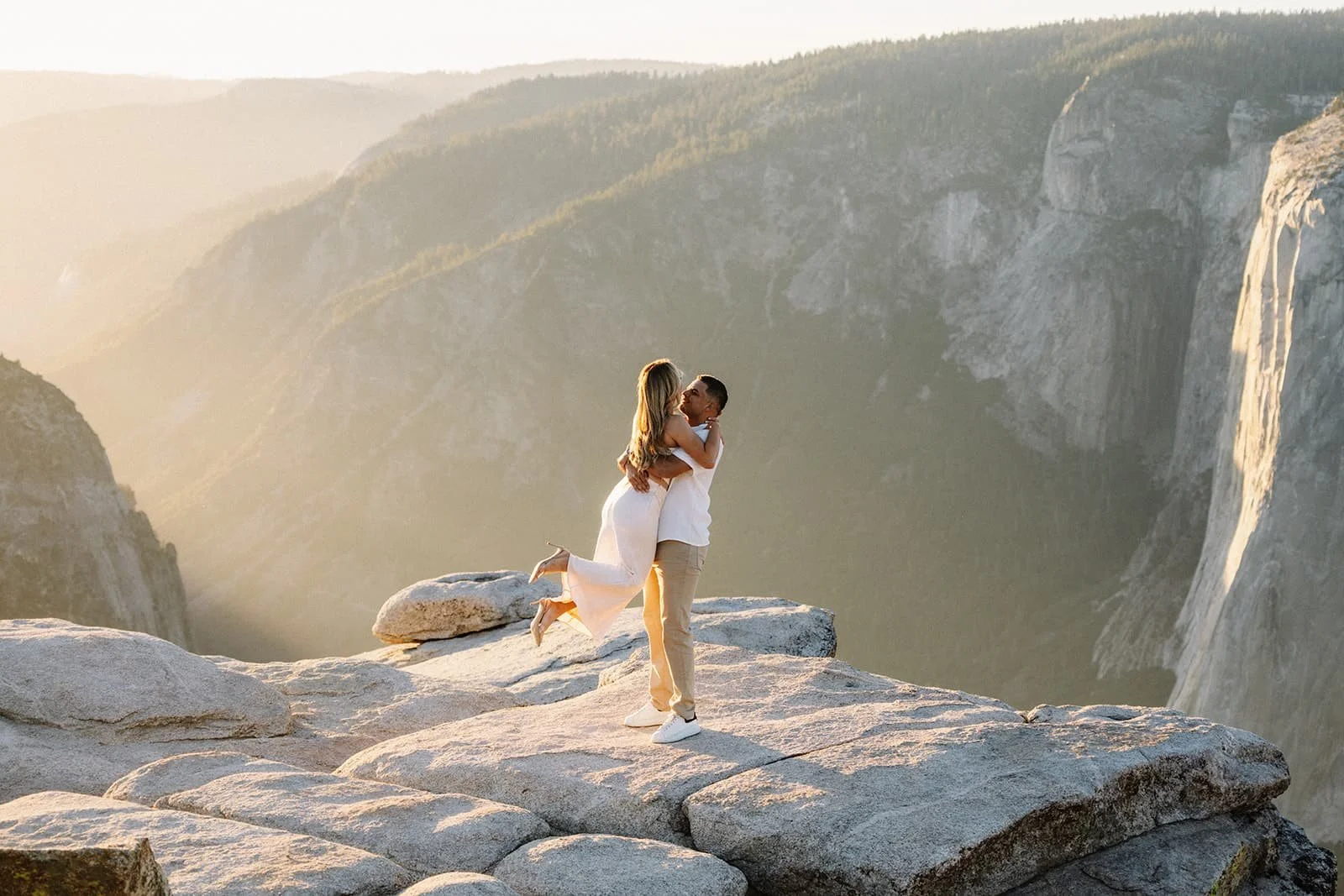 Couple embracing on a rocky ledge at Taft Point in Yosemite at sunset during their engagement session, high cliffs and valley in the background