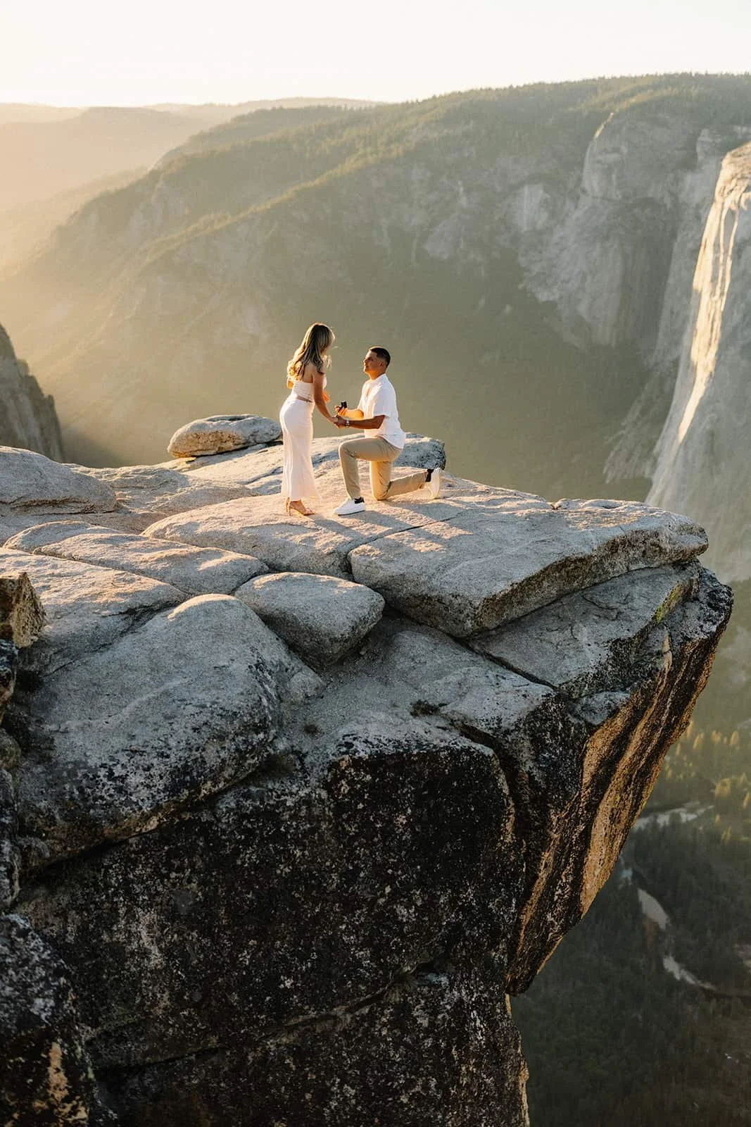 Couple sharing a marriage proposal on a rock ledge at Taft Point in Yosemite, mountain scenery at sunset