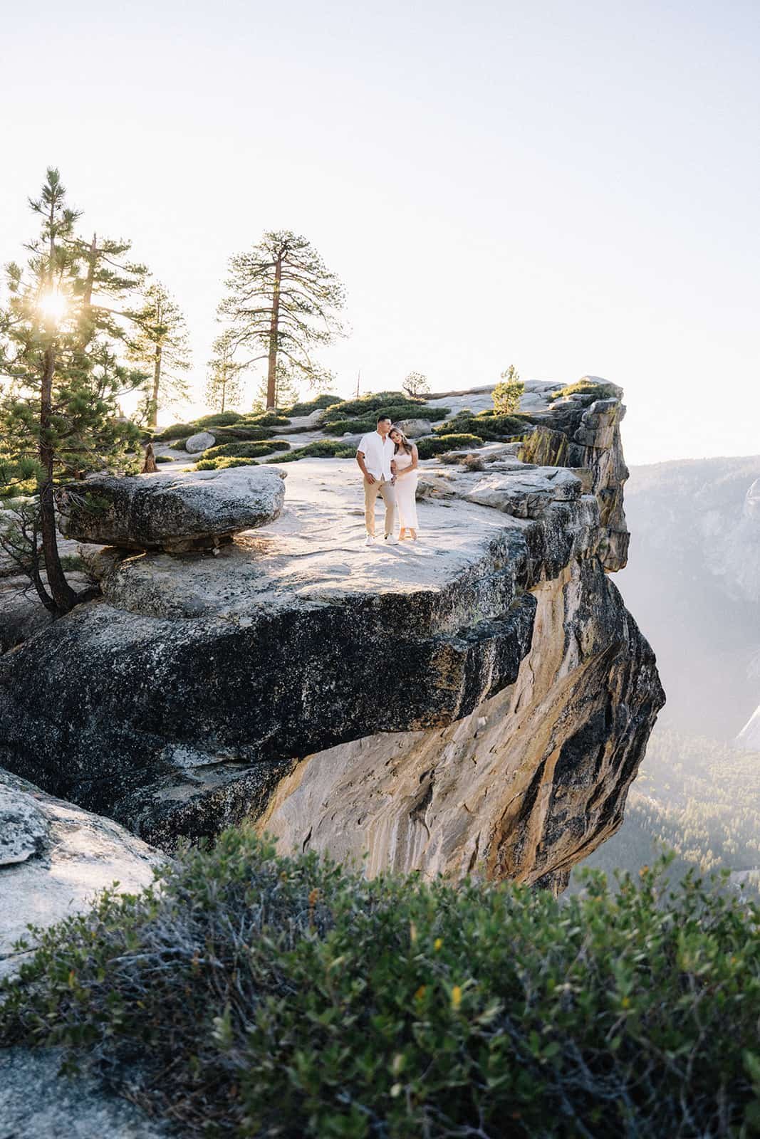 Couple holding hands on a rocky ledge at Taft Point in Yosemite, overlooking the canyon at sunset surrounded by trees