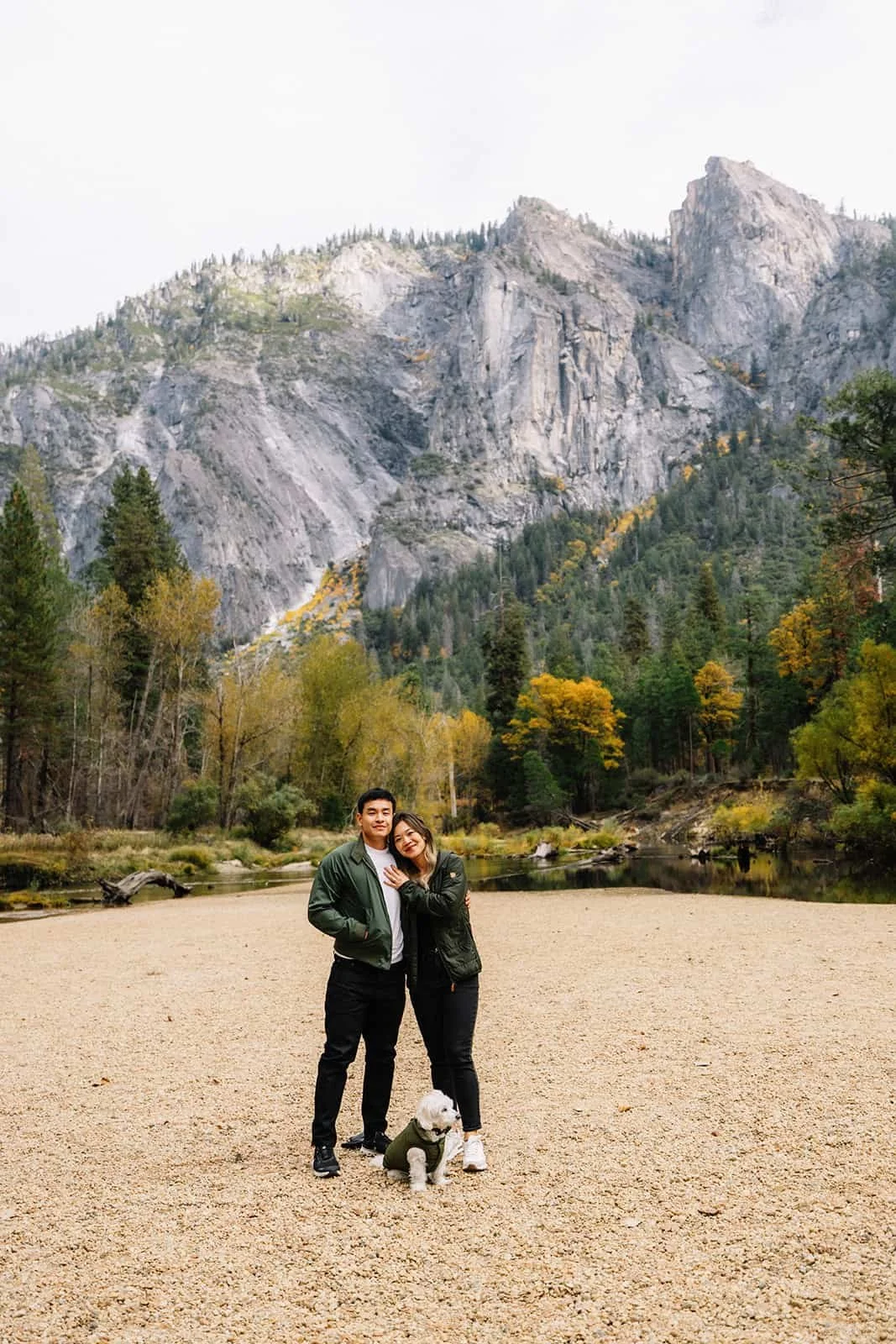 Couple with their dog standing on the sandy shore of Cathedral Beach in Yosemite, river and mountains in the background