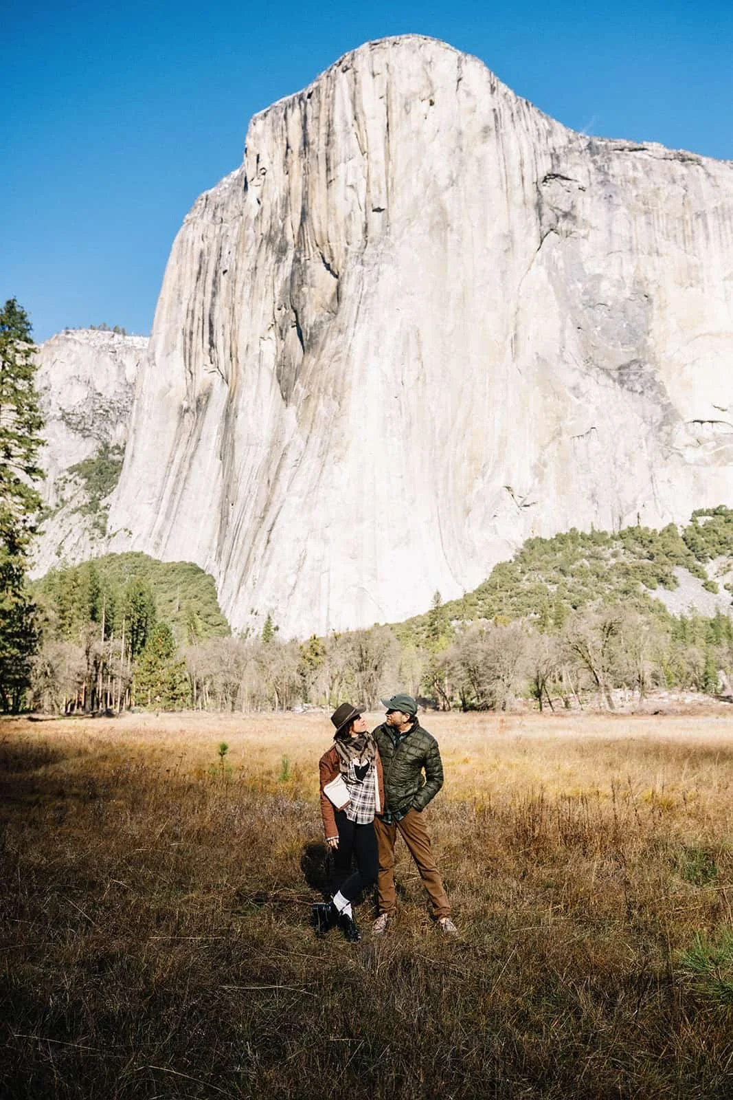 Couple standing in Cathedral Meadow in Yosemite with a El Capitan rising behind them under a clear blue sky