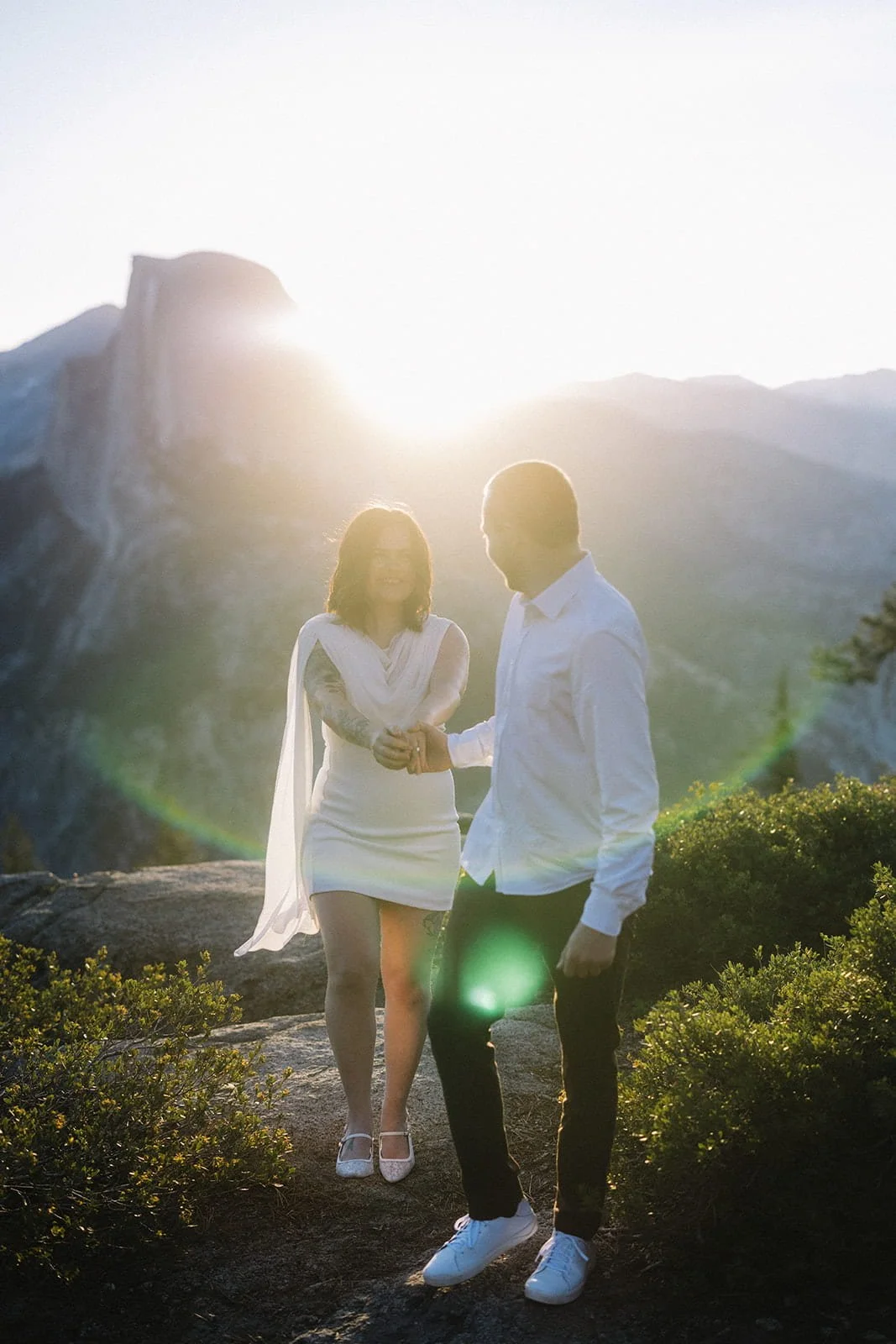 Couple holding hands and smiling at Glacier Point in Yosemite at sunset, mountains in the background