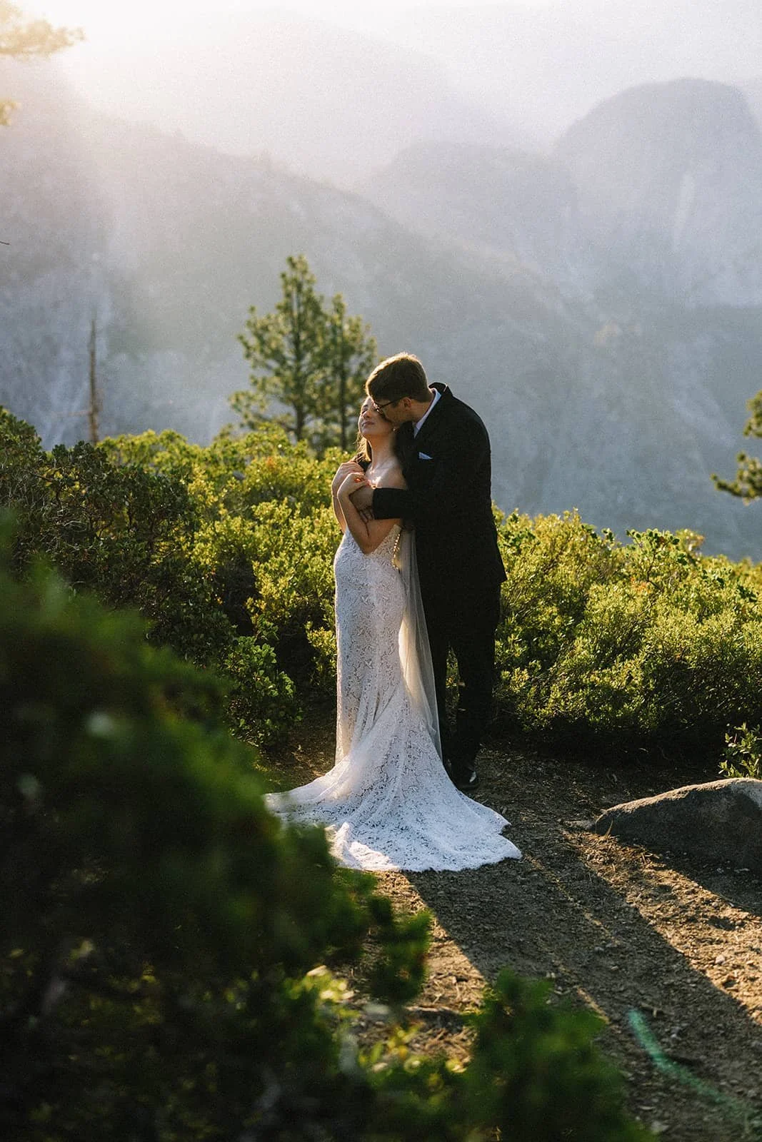 Couple embracing in golden morning light with mountain fog behind them at a Yosemite elopement