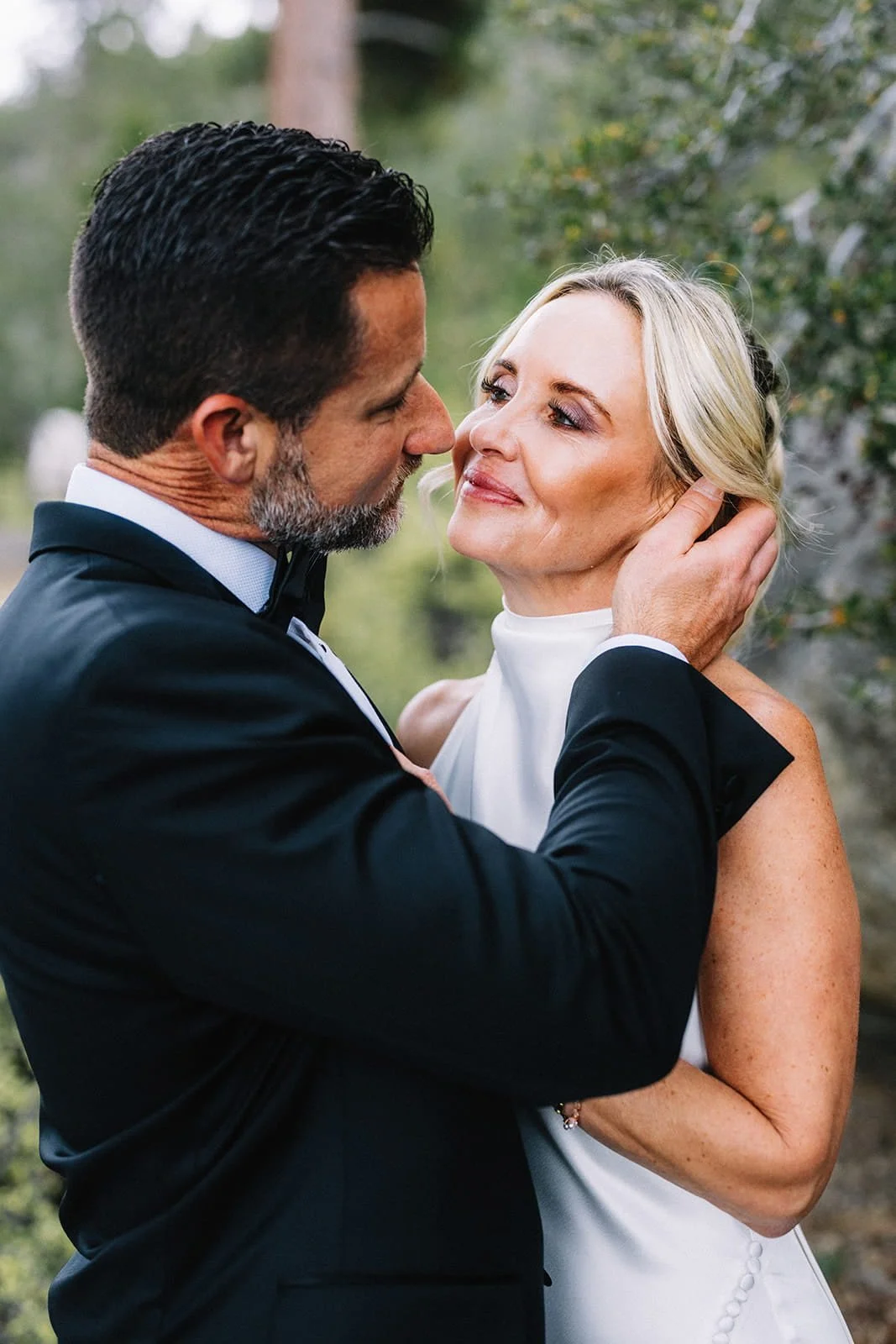 Close-up of the bride and groom embracing among pine trees.jpg