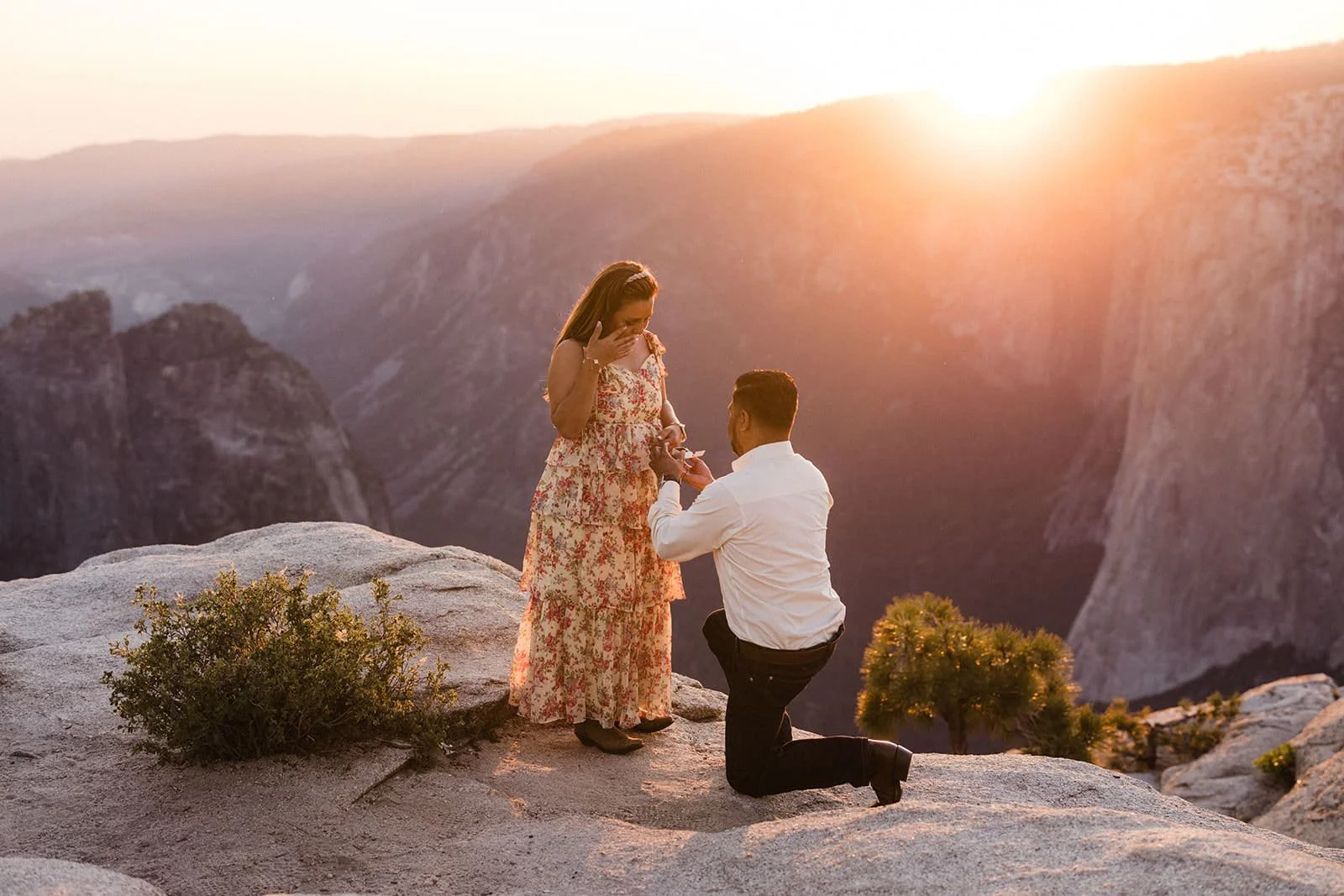 Man kneeling in proposal on a rocky ledge at Taft Point in Yosemite at sunset, mountains in the background