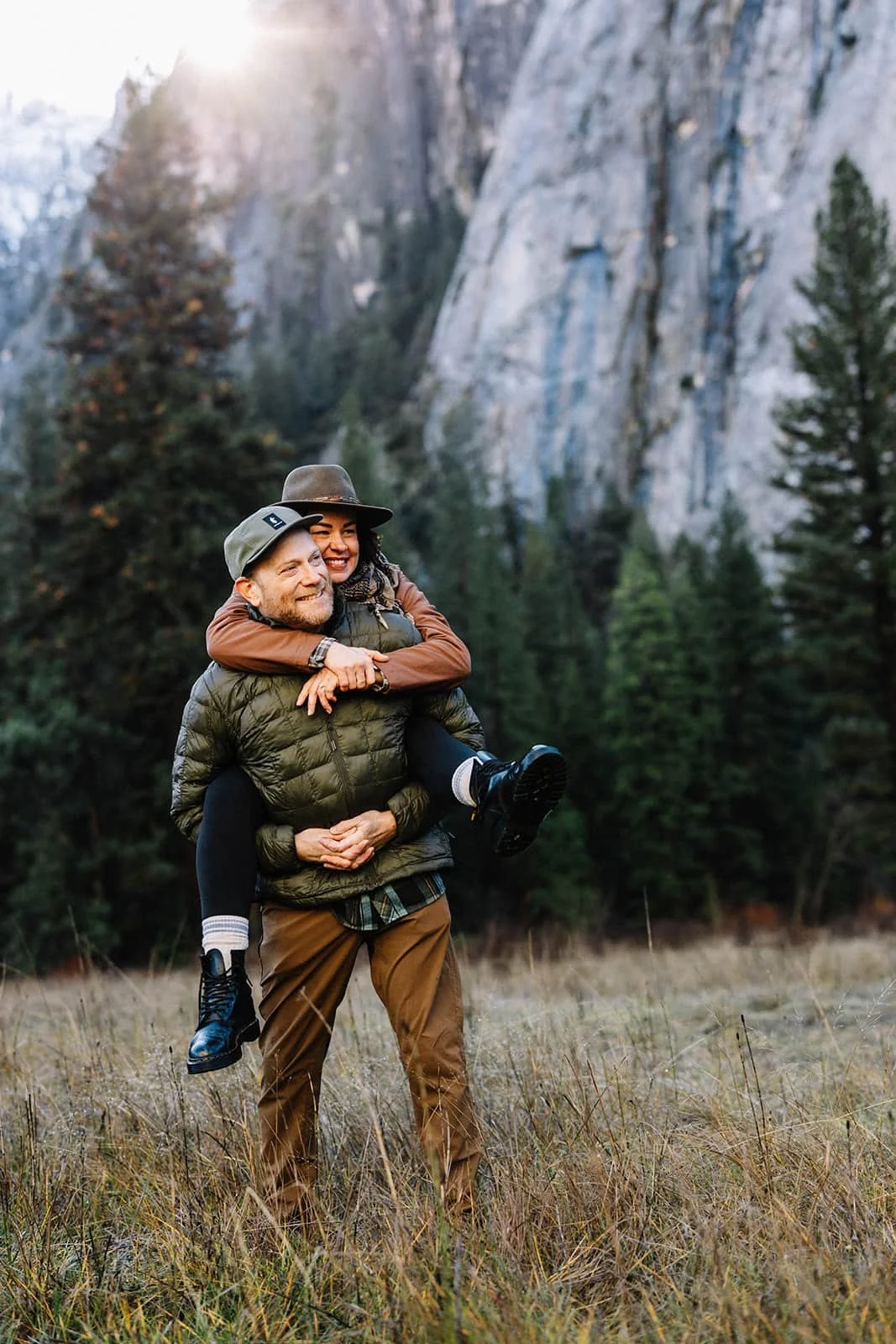 Couple hiking through Cathedral Meadow in Yosemite, the man carrying his partner on his back with mountains in the background