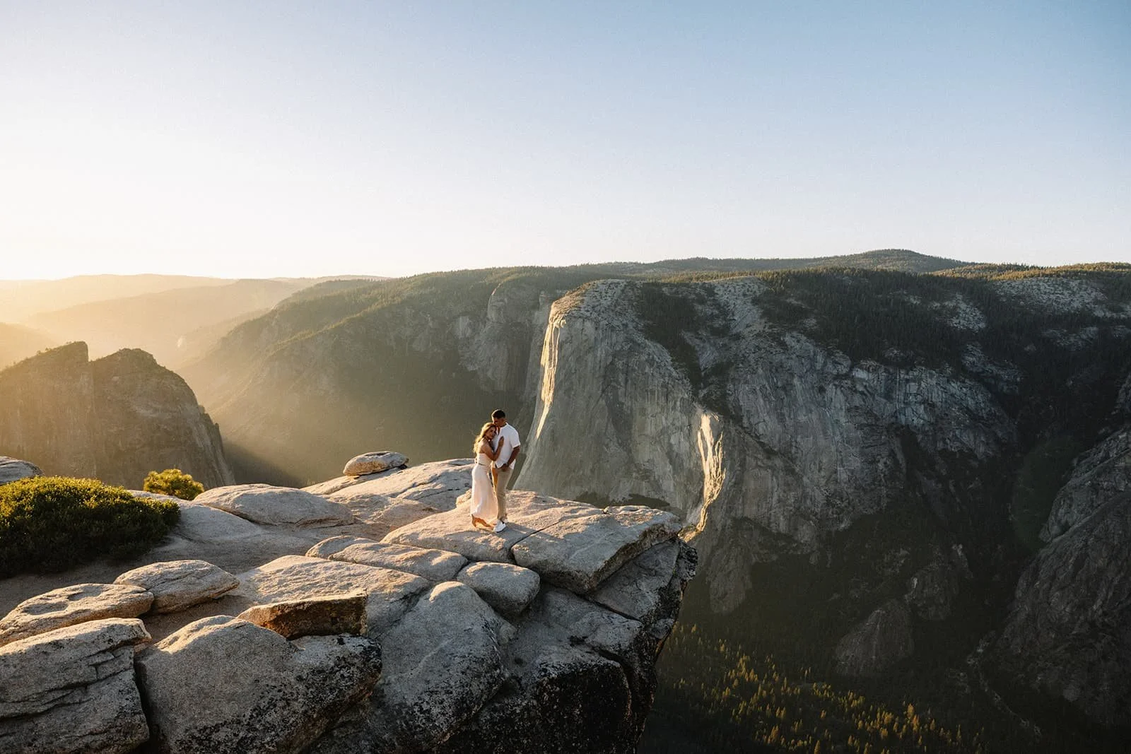 Couple embracing at a mountainous overlook at Taft Point during their Yosemite engagement session, valley and cliffs at sunset