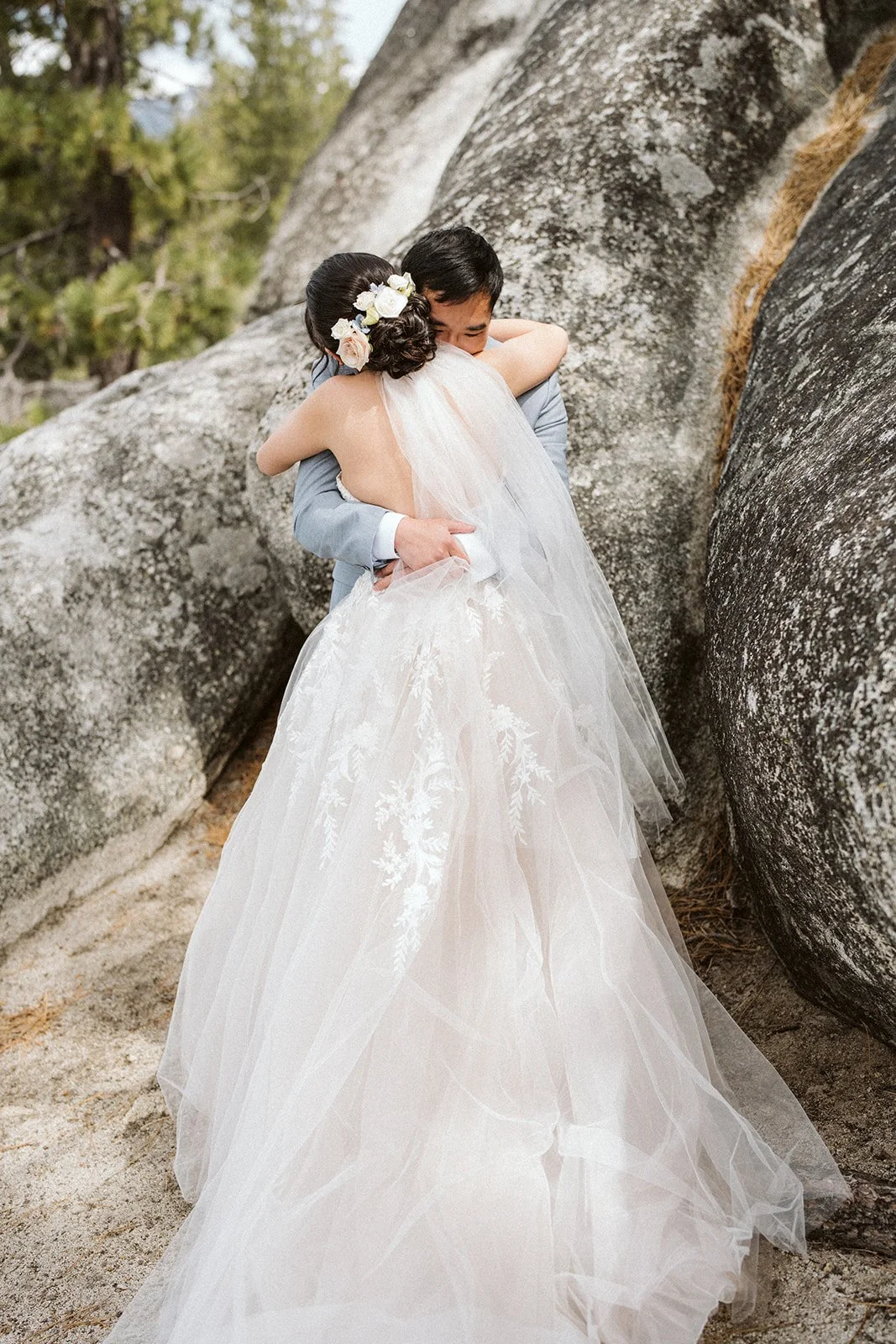 Couple hugging among granite boulders, bride in floral embroidery wedding dress, Lake Tahoe elopement — AJ Photography