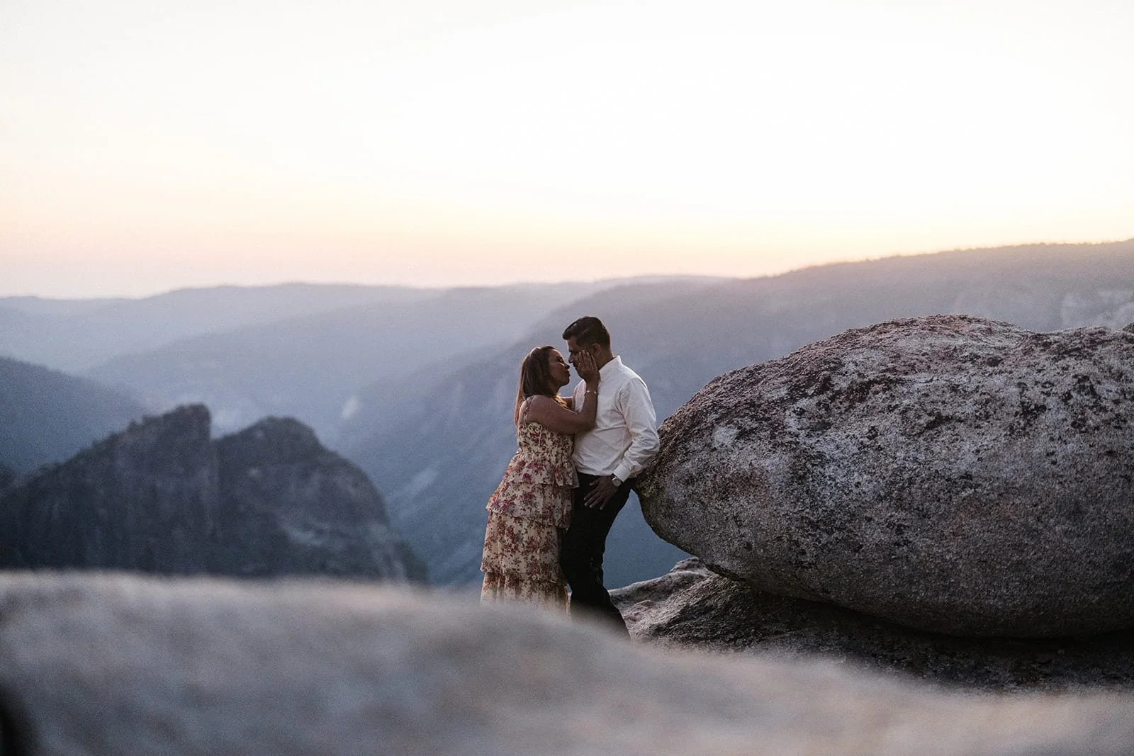 Couple standing close on a rock at Taft Point in Yosemite at sunset during their engagement session, the woman gently touching her partner's face