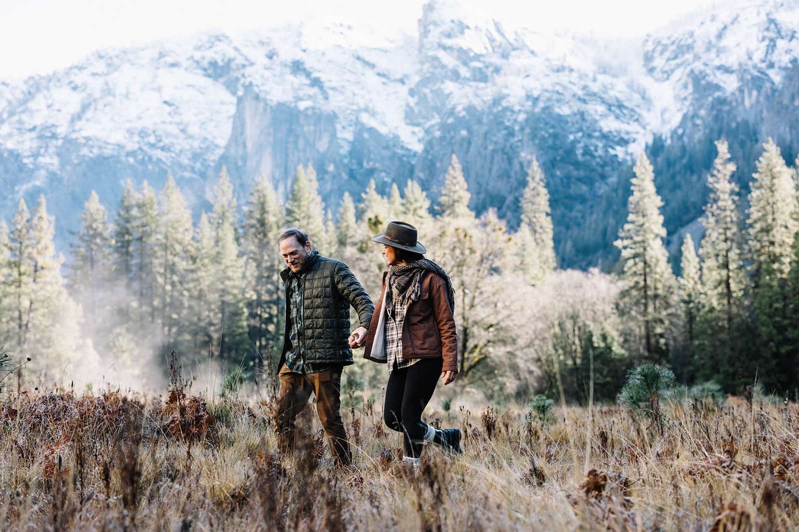Couple hiking through Cathedral Meadow in Yosemite during their engagement session, snow-capped peaks in the background