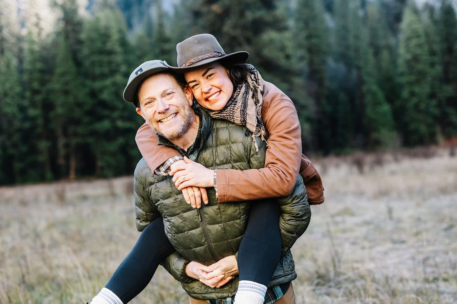 Man giving his partner a piggyback ride through the forest in Cathedral Meadow, Yosemite, both smiling