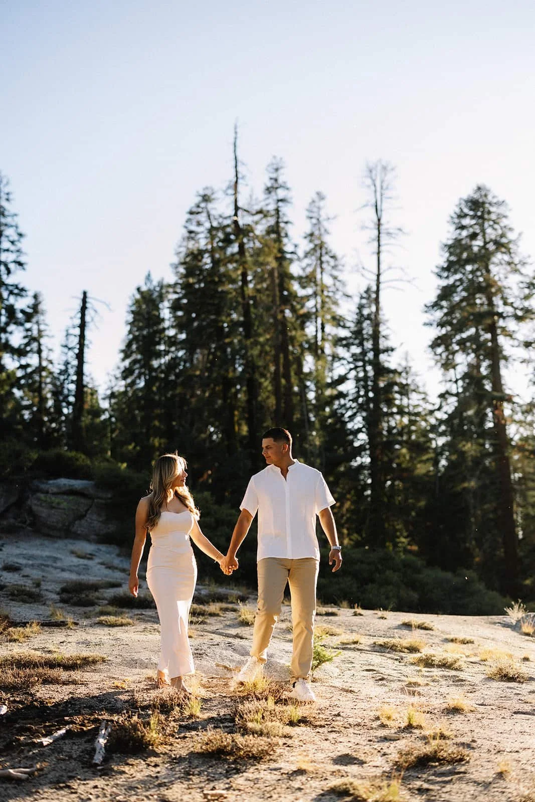 Couple holding hands and walking through the forest at Taft Point in Yosemite at sunset during their engagement session