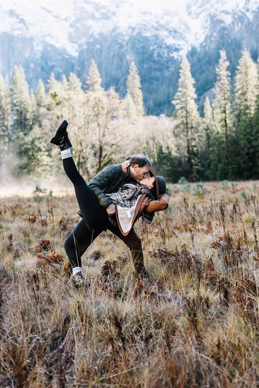 Man lifting his partner in a dance pose at Cathedral Meadow in Yosemite during their engagement session, trees and mountains in the background