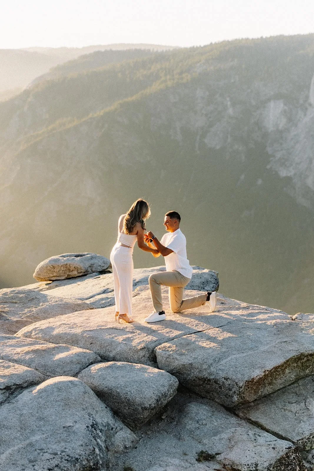 Man proposing to his partner on a rock at Taft Point in Yosemite during their engagement session, mountains at sunset in the background