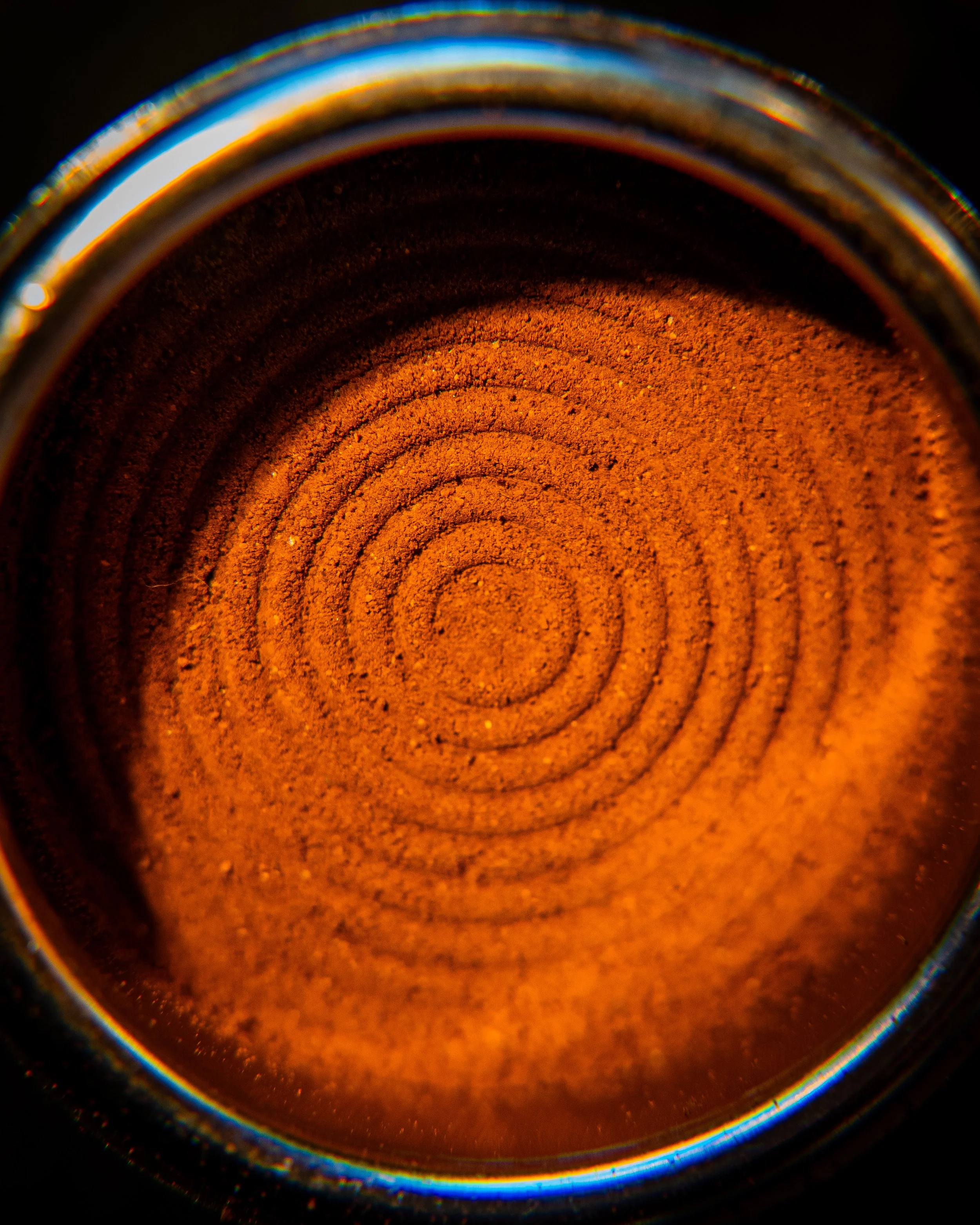 Close-up of the inside of a spice container filled with reddish-orange ground spice, with concentric rings and a reflective metal rim.