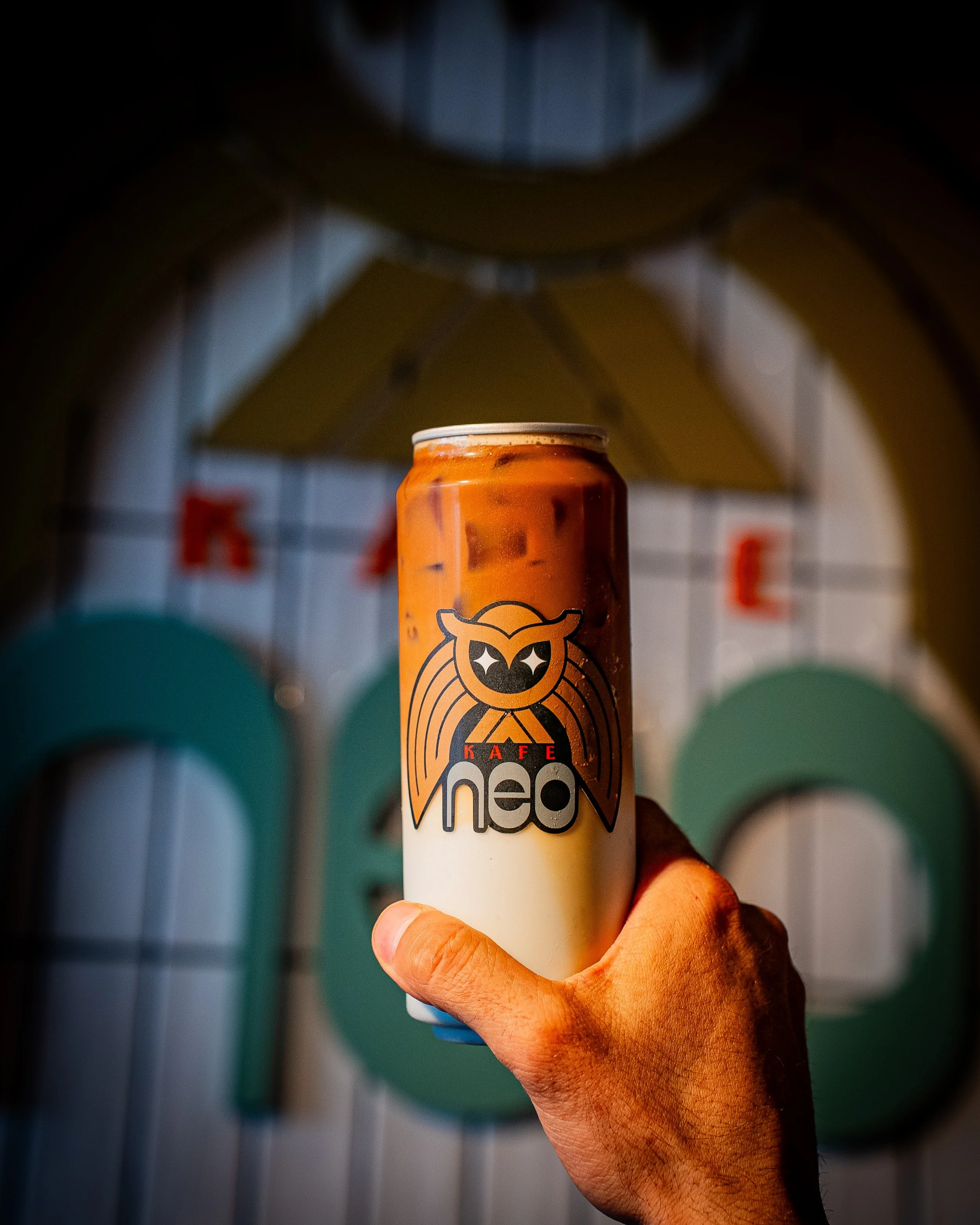 Close-up of a hand holding a can of KAFE Neo coffee drink against a background of colorful circles.