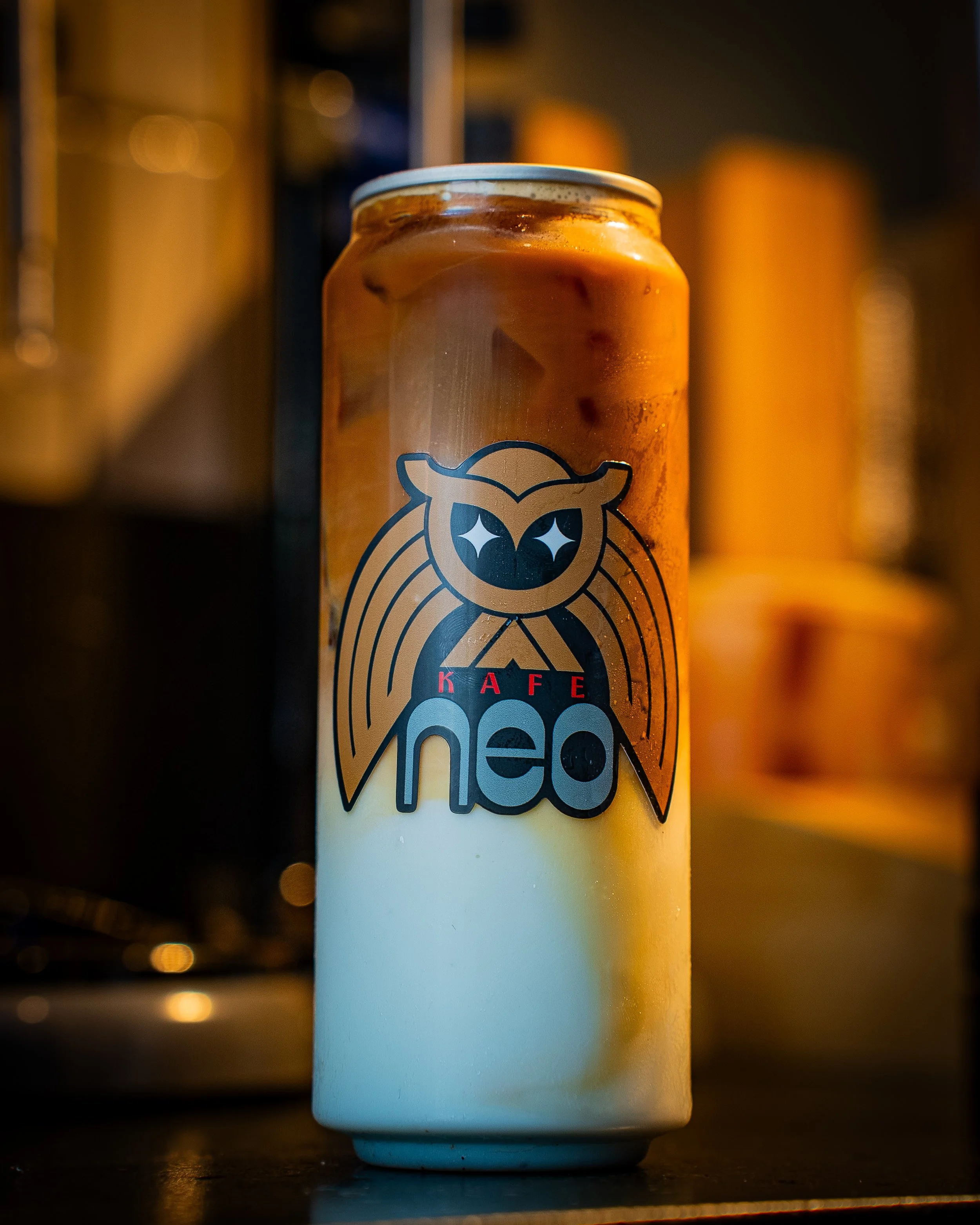 Close-up of a can with a logo of an owl, partially visible, on a white surface with blurred background lights.