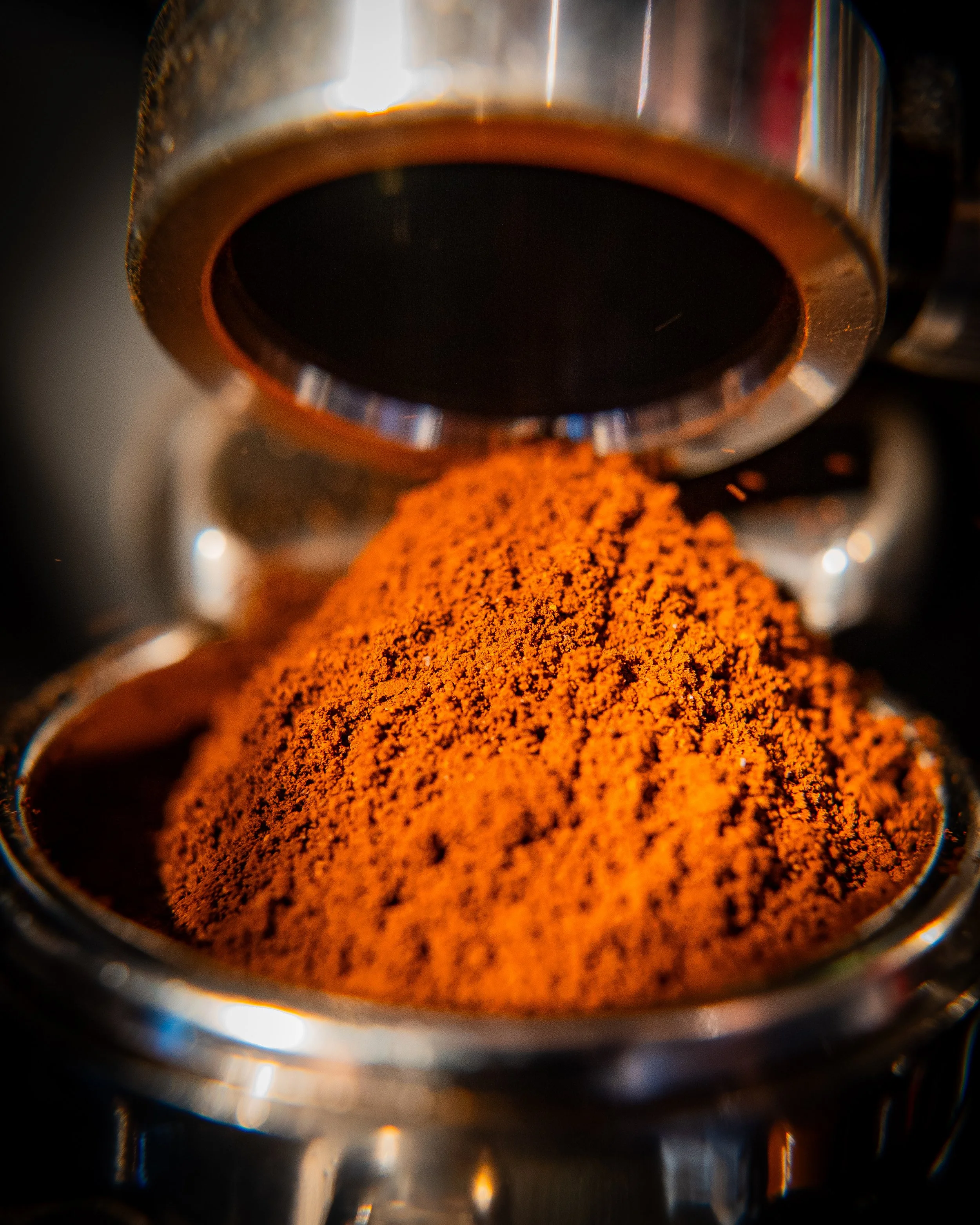 Close-up of a metallic coffee pot pouring ground coffee into a cup.