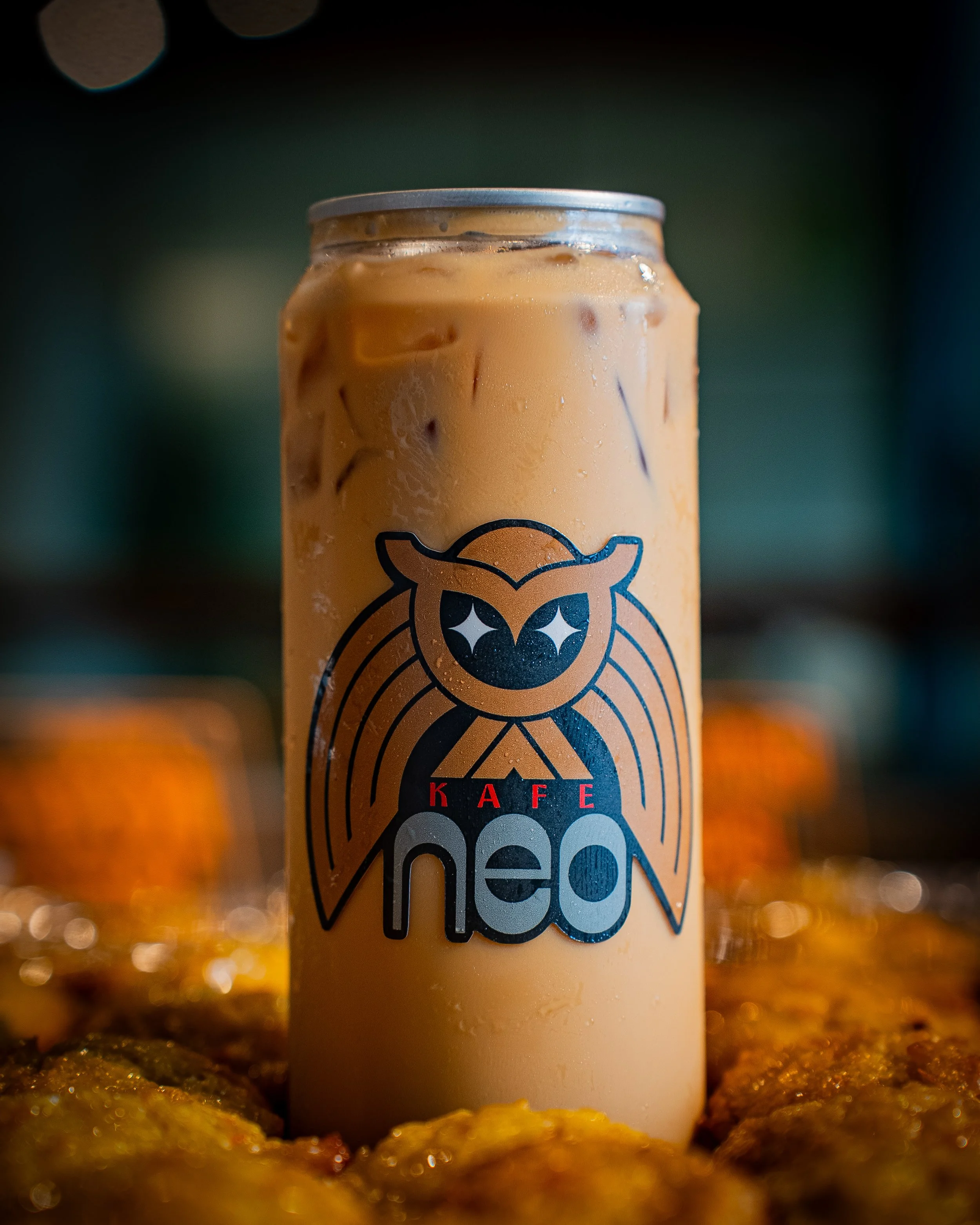 Close-up of a can of coffee with a cartoon animal logo, set against a blurred background with orange objects in the foreground.