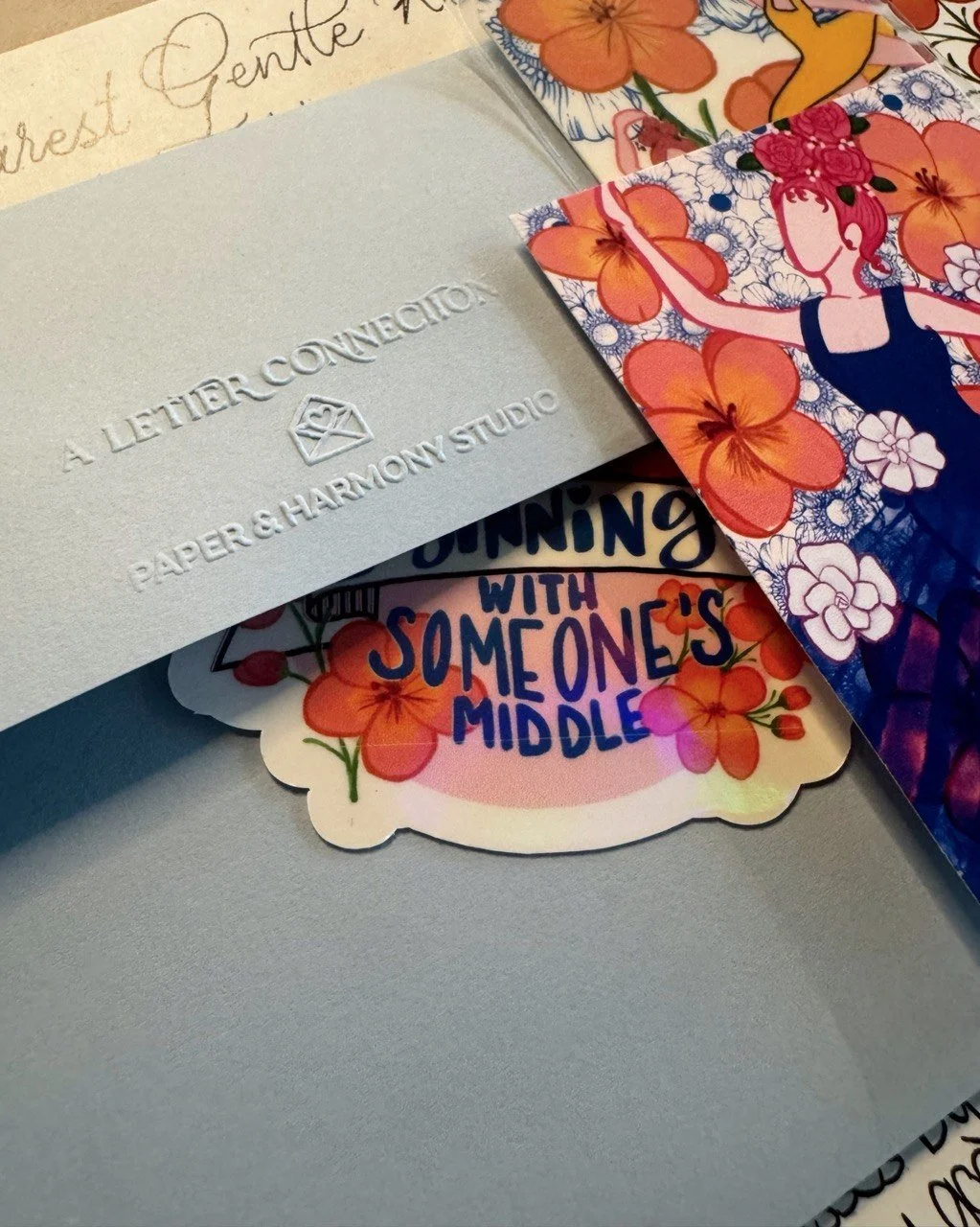 A detailed close up of blue envelope embossed with A Letter Connection by Paper & Harmony, an original art sticker and bookmark peeking on the side and underneath envelope flap.