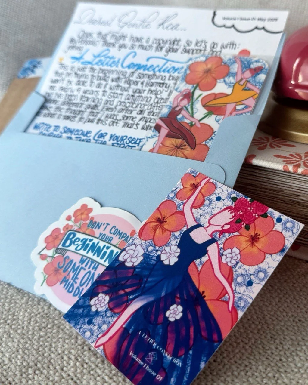 Issue 01 of A Letter Connection, a handwritten letter with doodles peeking out of a blue envelope, with themed bookmark, sticker, and ATC included