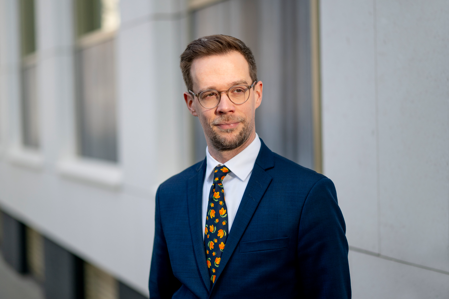 Rechtsanwalt Christoph Trafoier trägt einen blauen Anzug, Brille und eine bunte Krawatte.