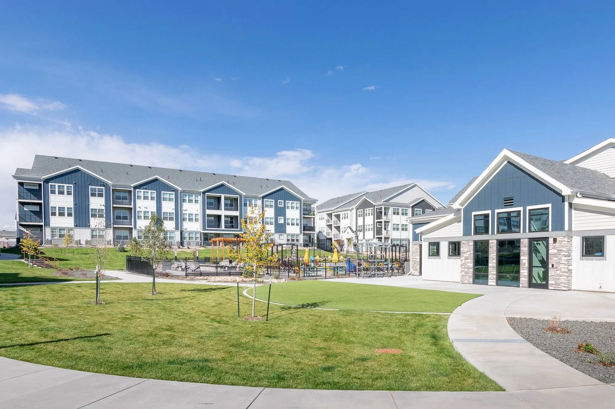 Lariat multifamily complex with multi-story blue and white buildings, a landscaped grassy area, and a playground.