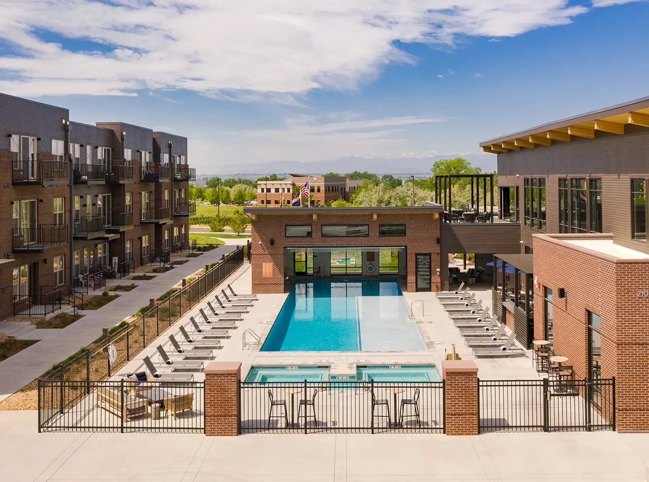 Railway Flats apartment complex with a central swimming pool surrounded by lounge chairs, sitting areas, and multiple apartment buildings, with greenery and mountains in the background.