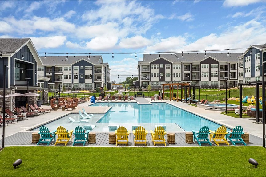 Lariat apartment complex with a large swimming pool, surrounded by colorful Adirondack chairs, umbrellas, and with multi-story residential buildings in the background.