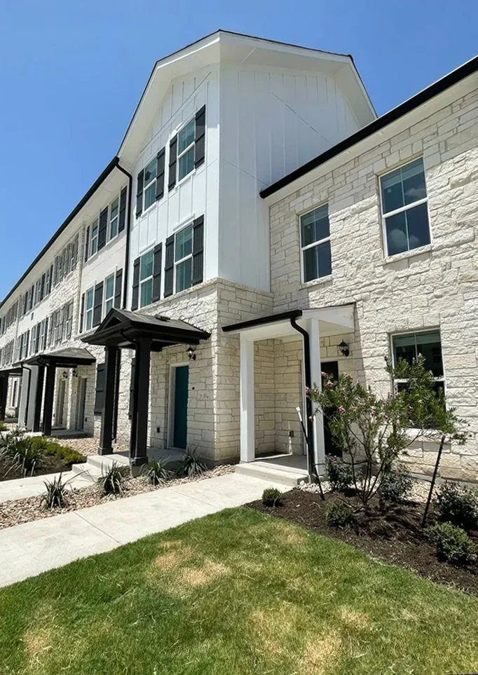 LC Pflugerville multifamily white multi-story residential building, a small front yard, and clear blue sky.