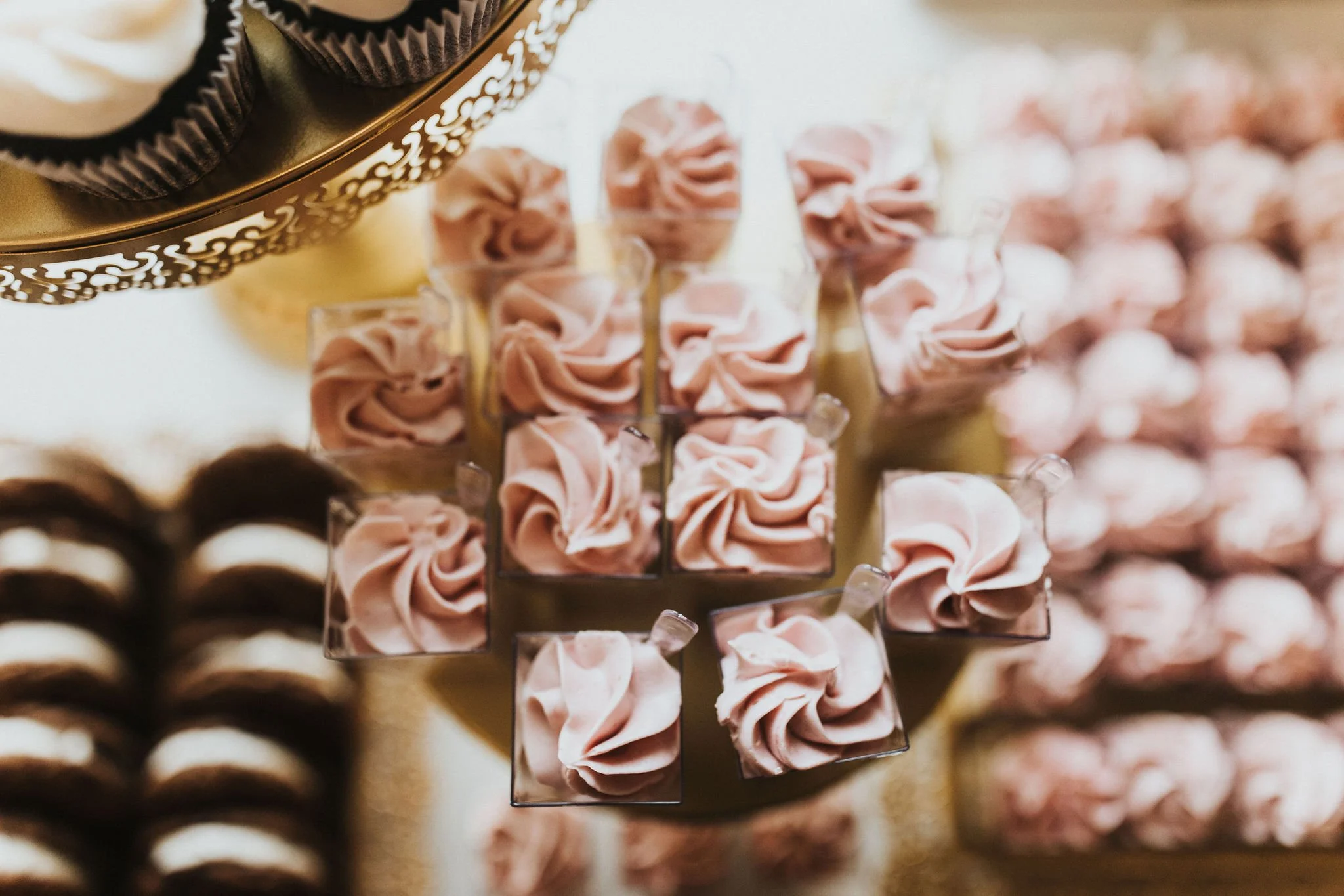Assorted small desserts arranged on a tiered tray, featuring pink and chocolate-colored treats.