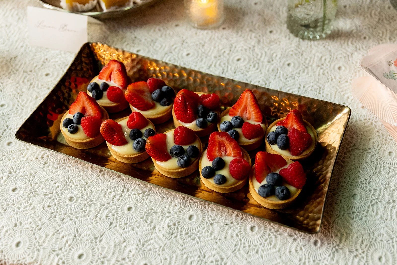 Small fruit tarts topped with strawberries, blueberries, and raspberries on a decorative silver tray