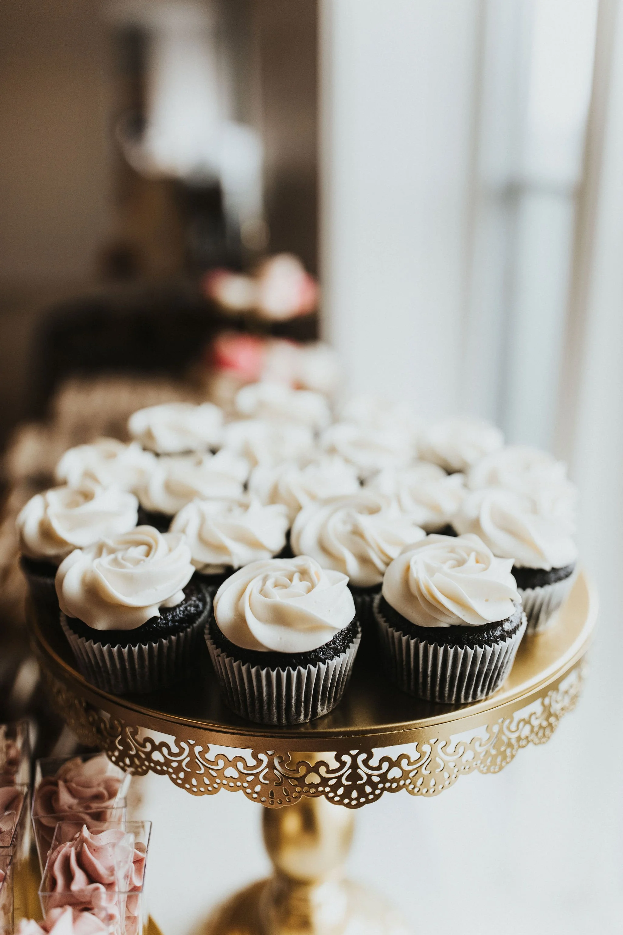 Chocolate cupcakes with white frosting rosettes on a gold ornate cake stand.