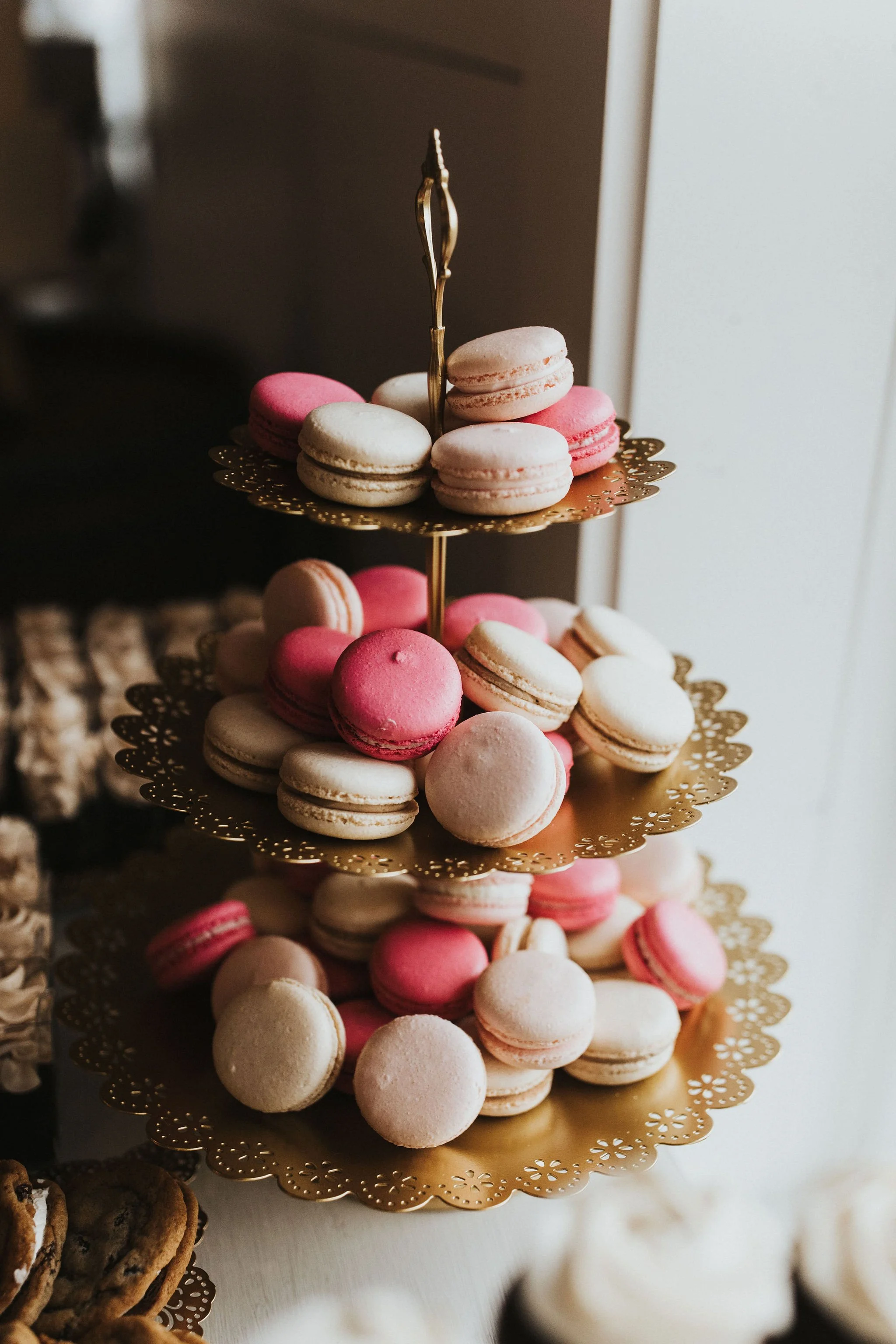 A three-tiered gold tray filled with pink and white macarons.