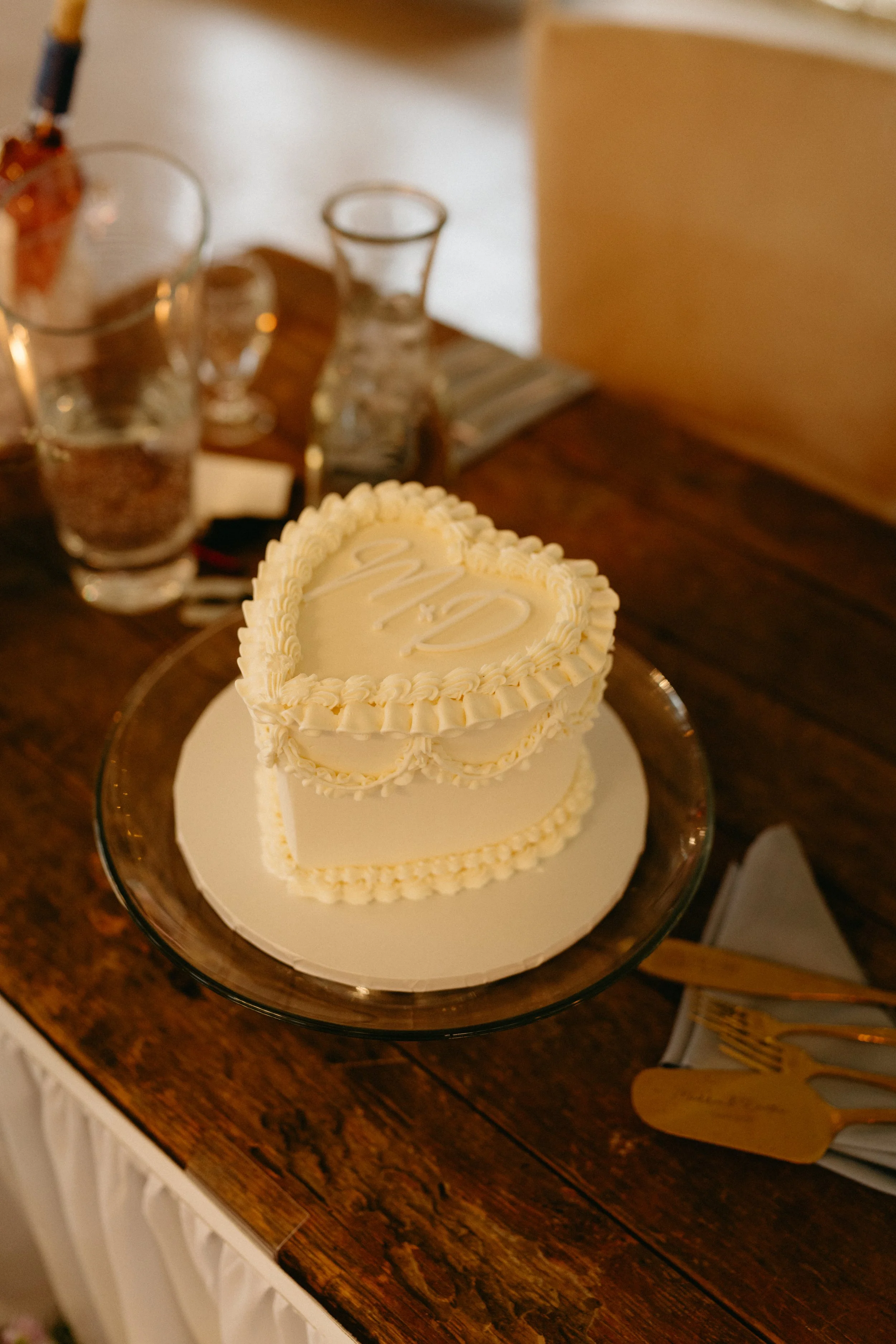 Heart-shaped wedding cake with white frosting and decorative borders on a glass cake stand.