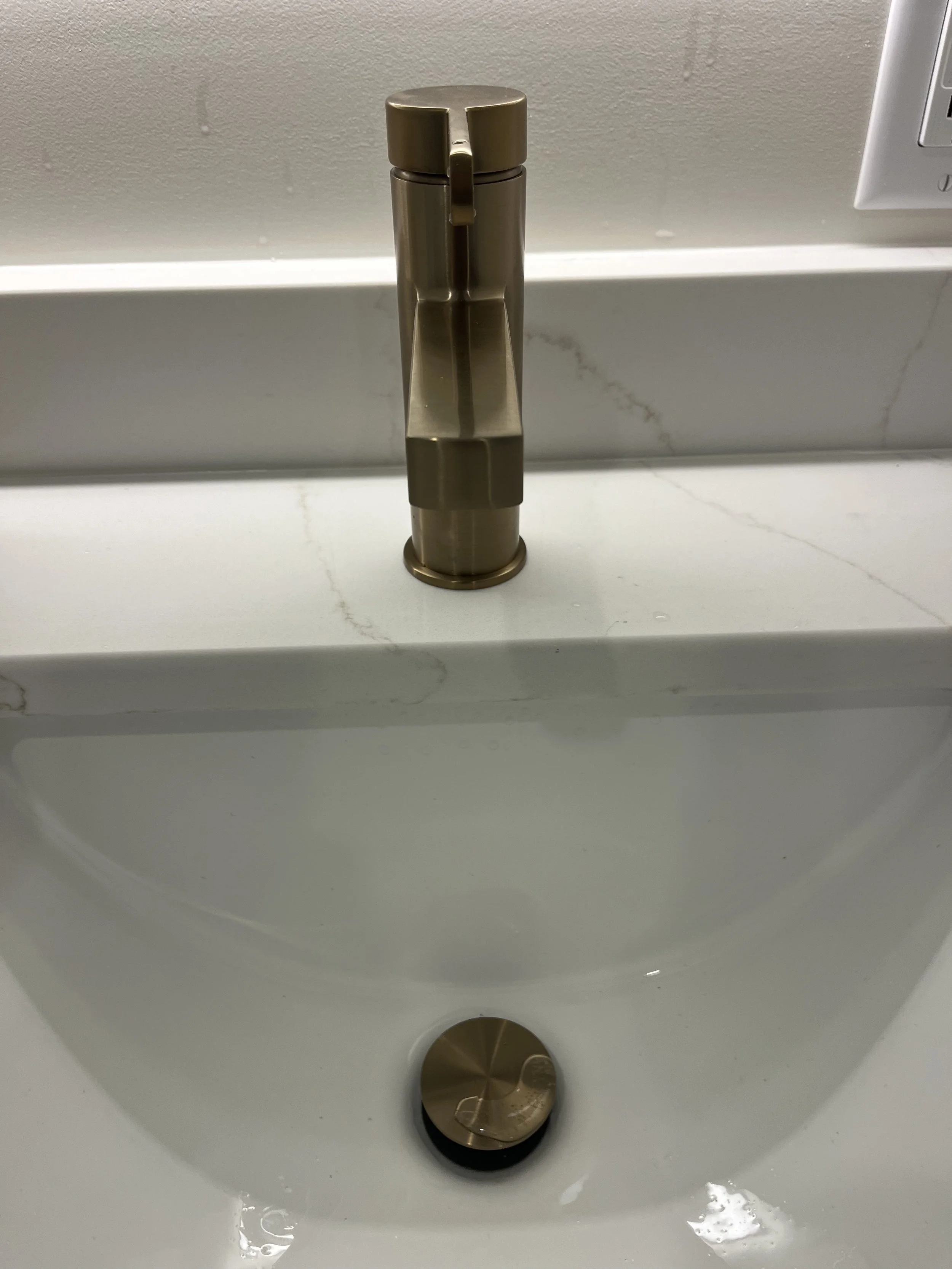 Brass-colored sink faucet above a white sink with a brass drain cover.