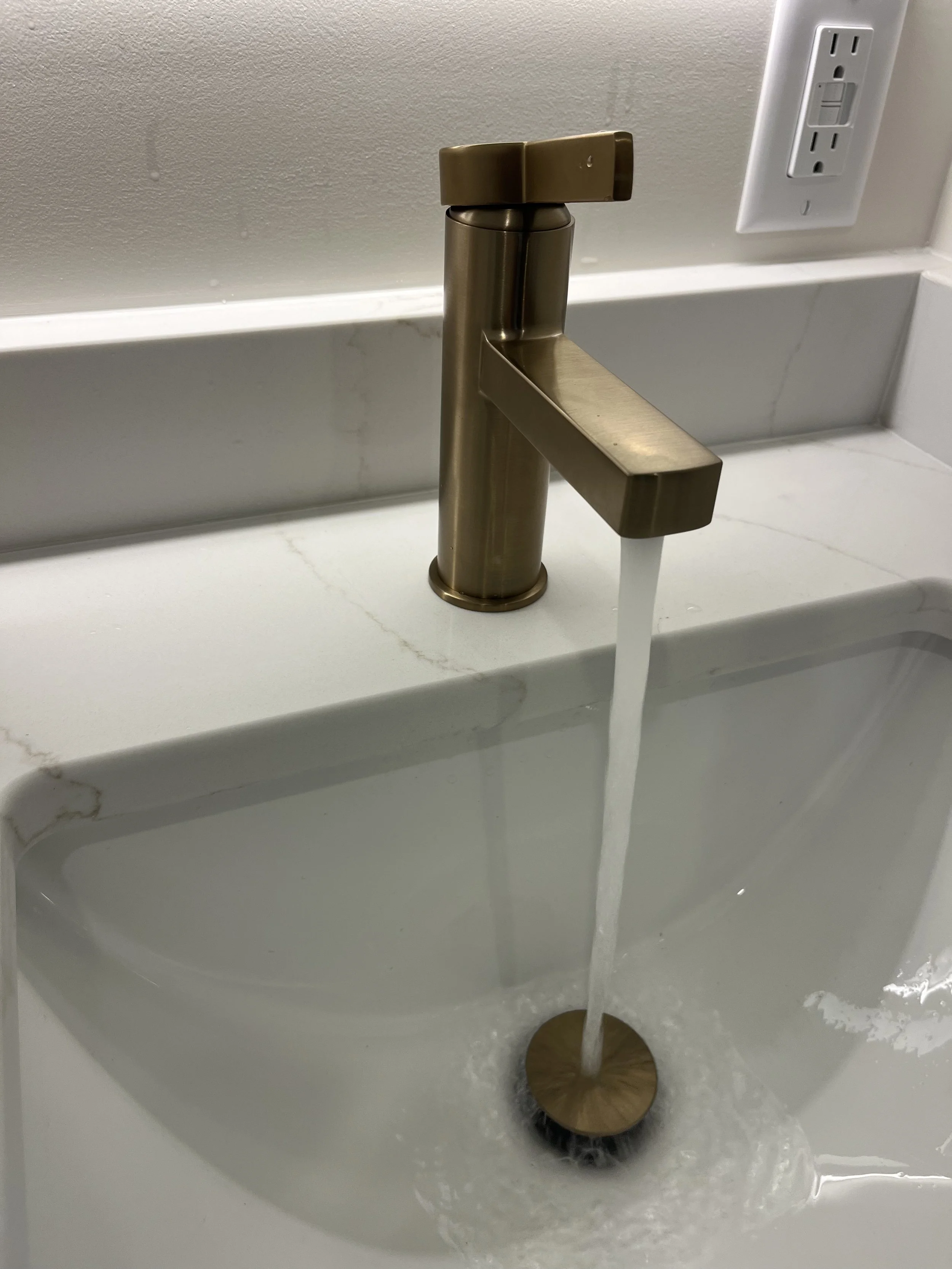 A modern gold-colored faucet with water flowing into a white marble sink.