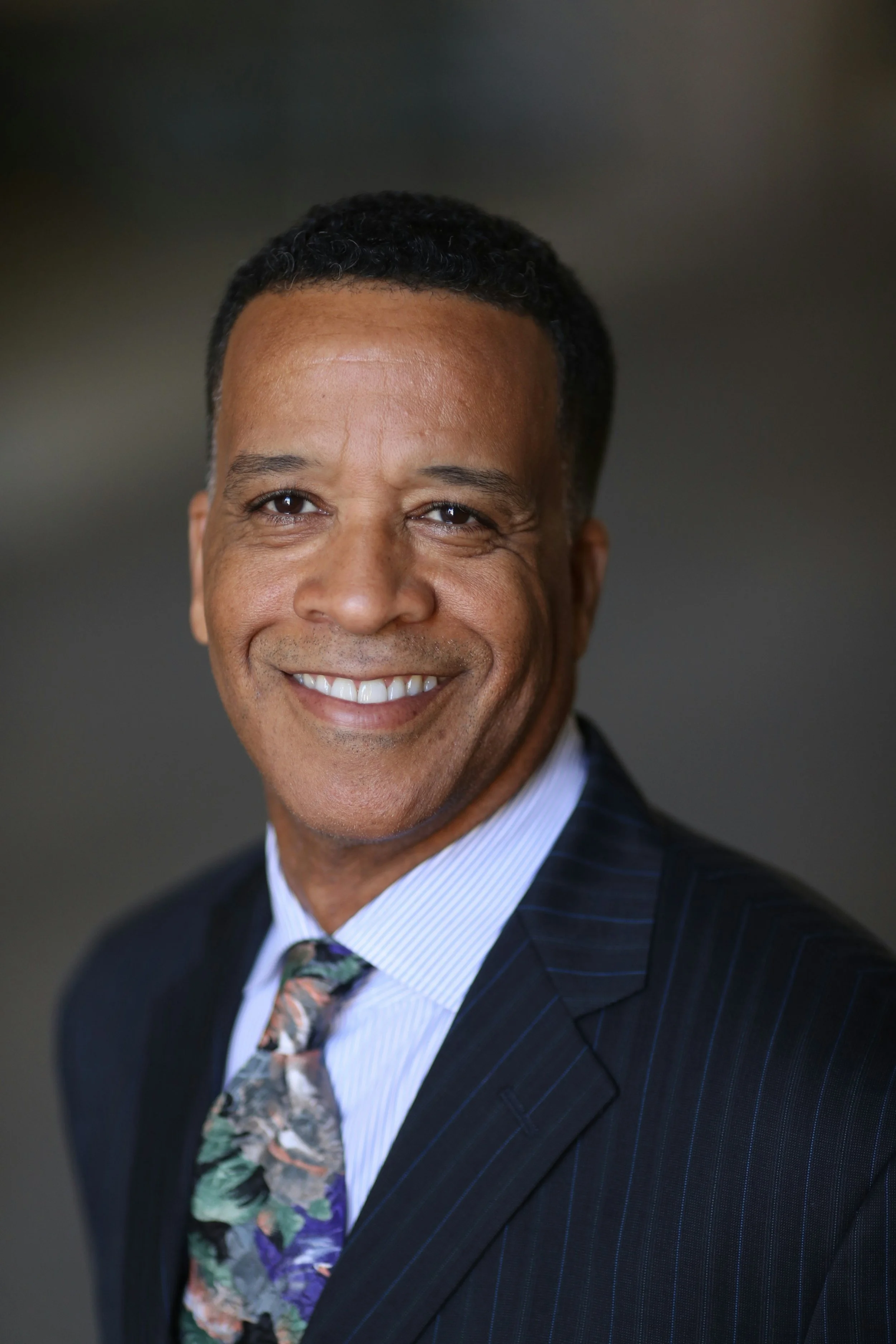 Close-up of a smiling African American man wearing a suit, dress shirt, and a colorful floral tie.