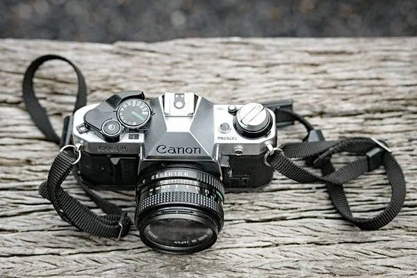 A Canon film camera with a lens, placed on a weathered wooden surface.
