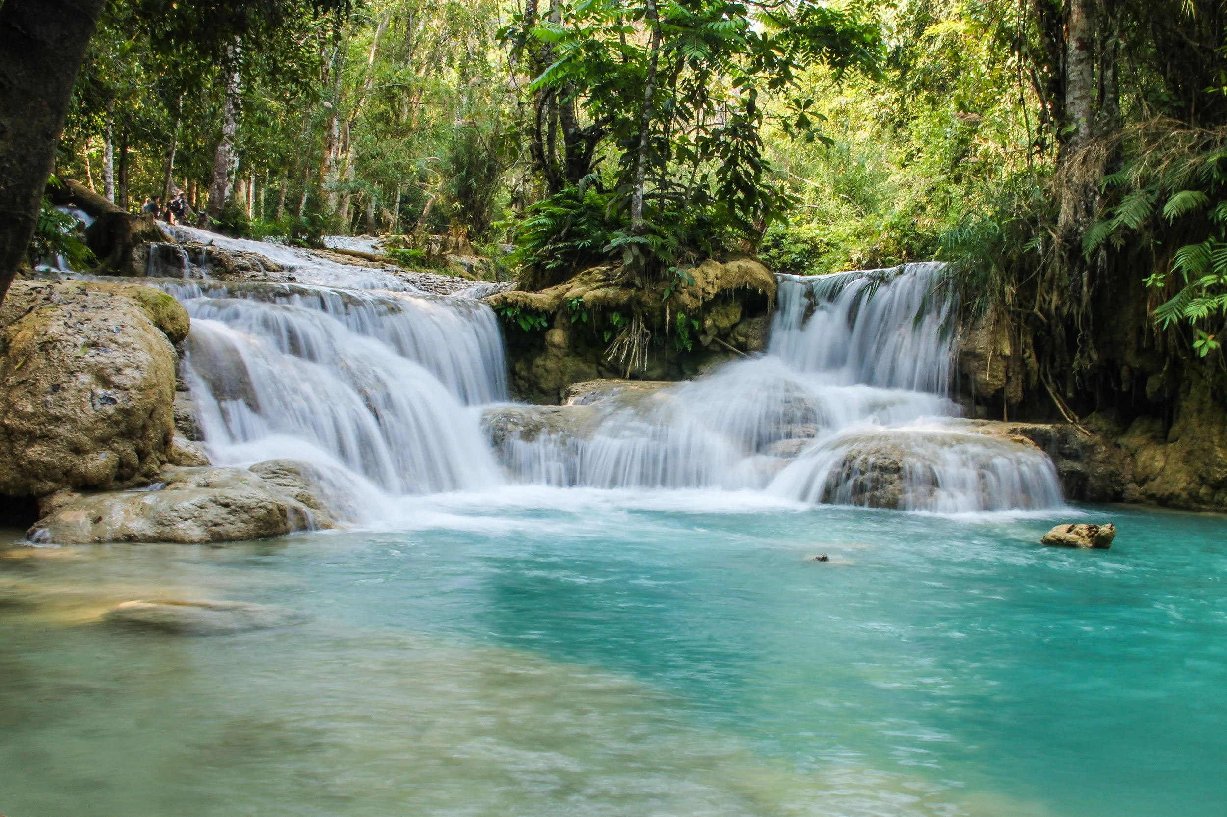 Kuang Si Waterfalls cascading into a turquoise pool with silky smooth water from slow shutter speed, surrounded by lush jungle foliage, Luang Prabang, Laos