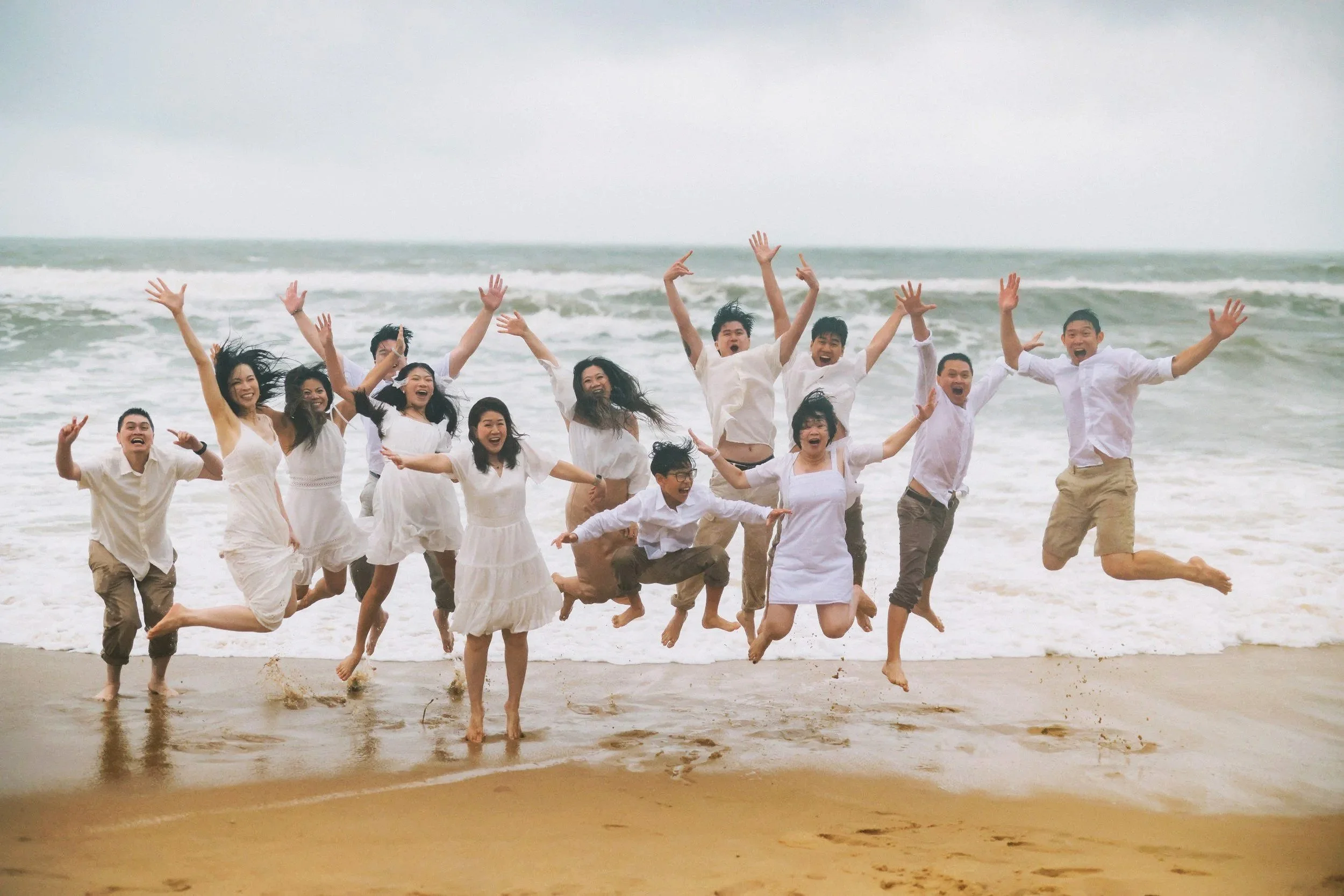 Group of wedding guests in white outfits jumping together on a tropical beach, Southeast Asia destination wedding