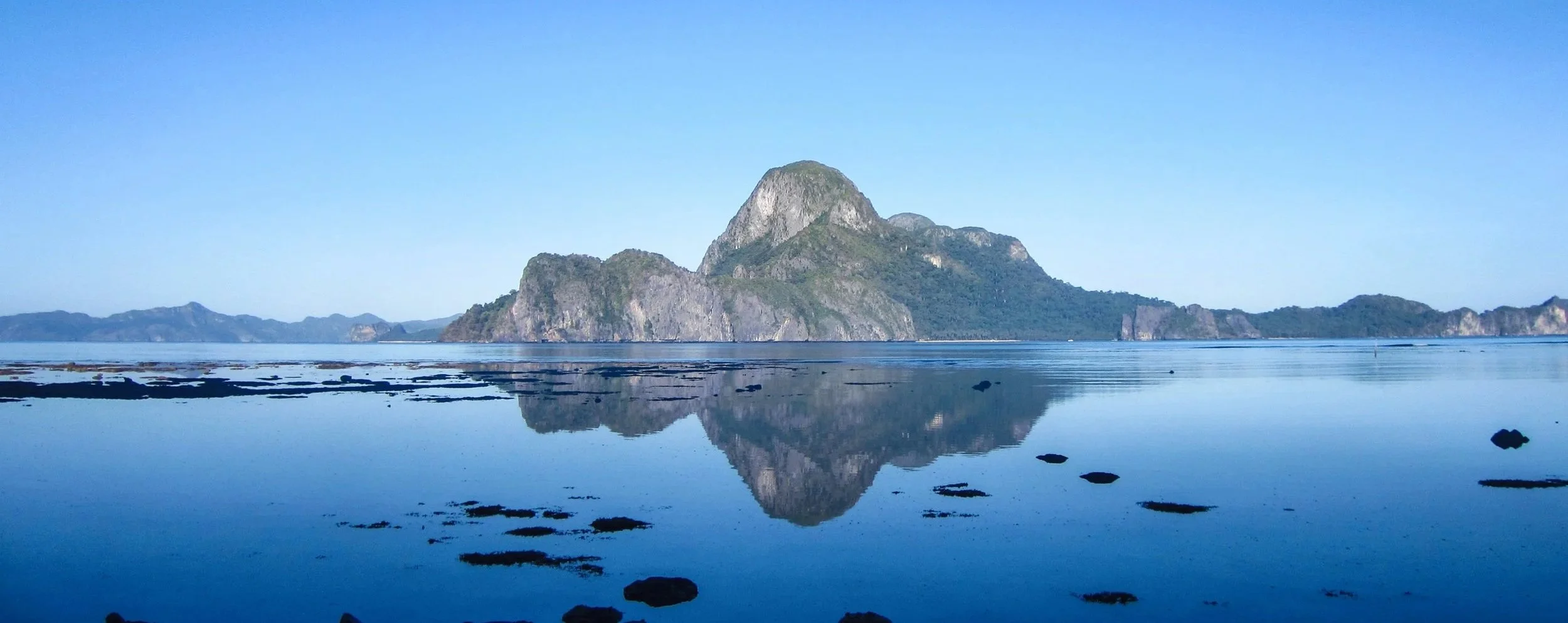 Cadlao Island perfectly reflected in the glassy calm waters of El Nido at early morning under a cloudless sky, Palawan, Philippines