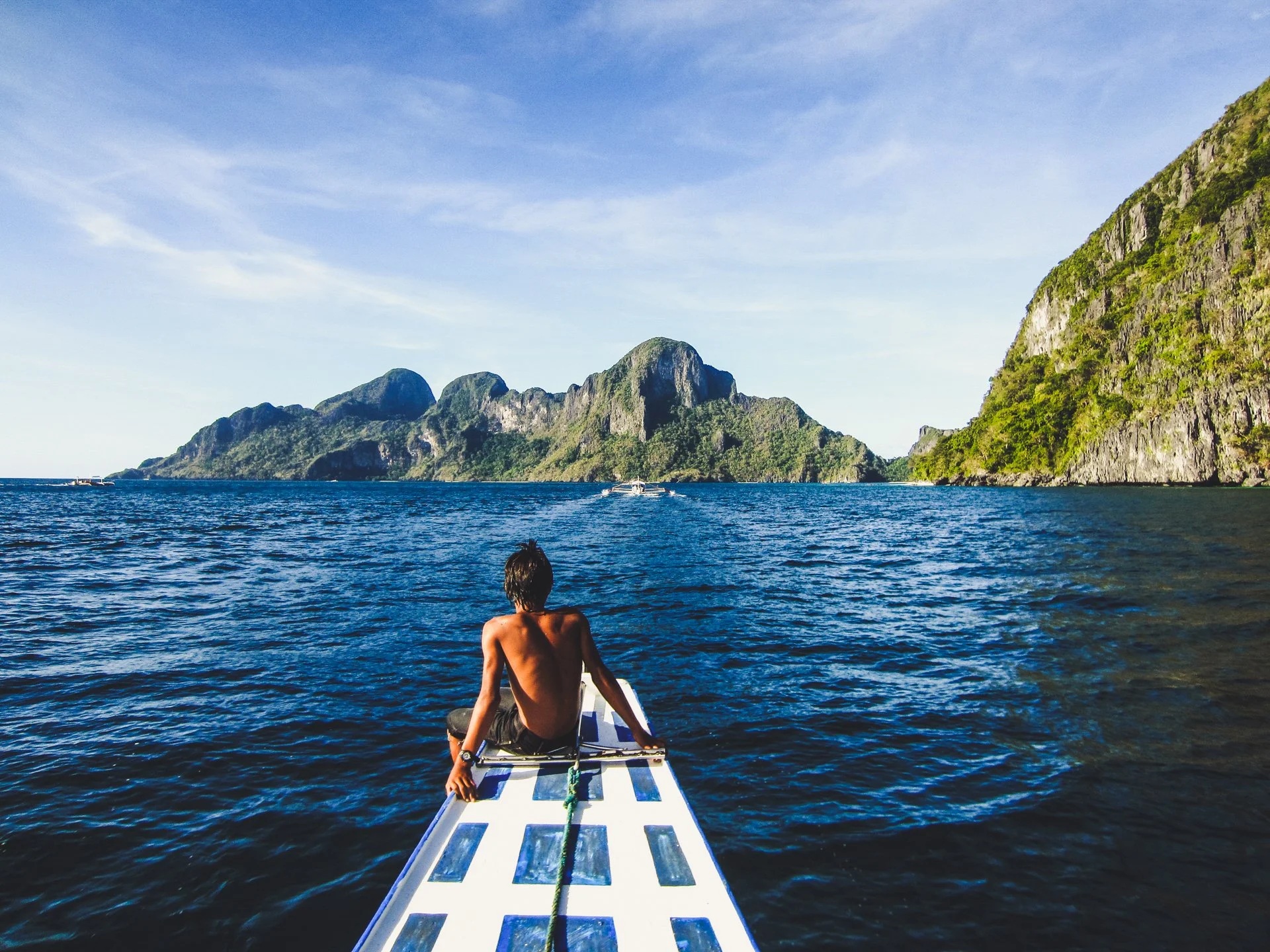Boat bow with traveler overlooking turquoise waters and limestone islands, El Nido, Philippines