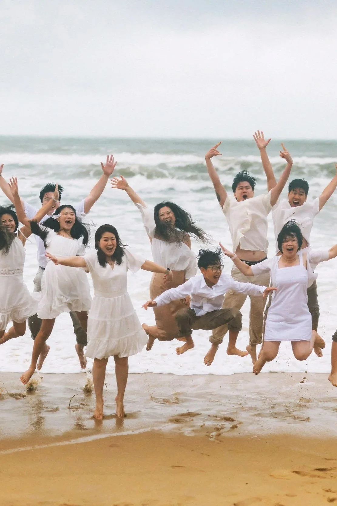 Group of wedding guests in white outfits jumping together on a tropical beach, Southeast Asia destination wedding