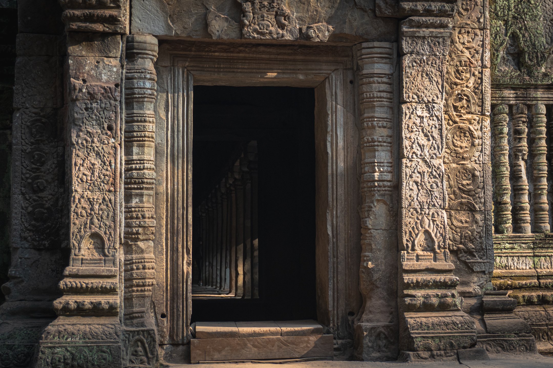 Ancient carved stone doorway at Angkor Wat, Cambodia, with shafts of sunlight cutting through the darkness