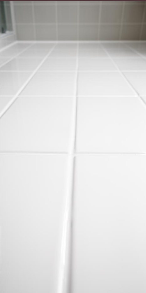 Close-up view of white ceramic bathroom tiles on the floor with grout lines.
